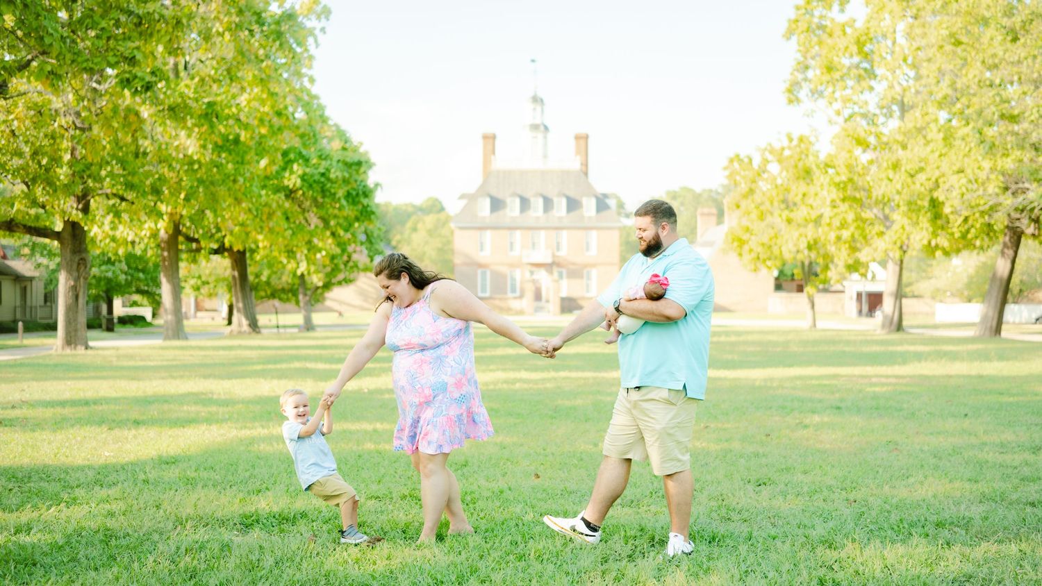 A family of three runs and plays together on a sunny lawn with a stately mansion in the background.
