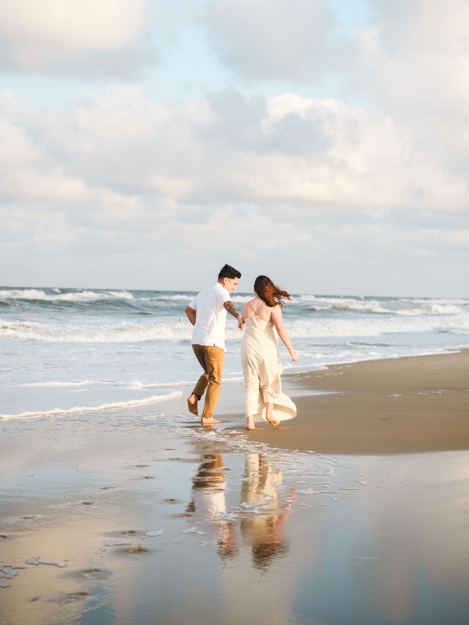 Couple strolling together along a scenic beach shoreline during sunset with gentle waves and reflective wet sand.