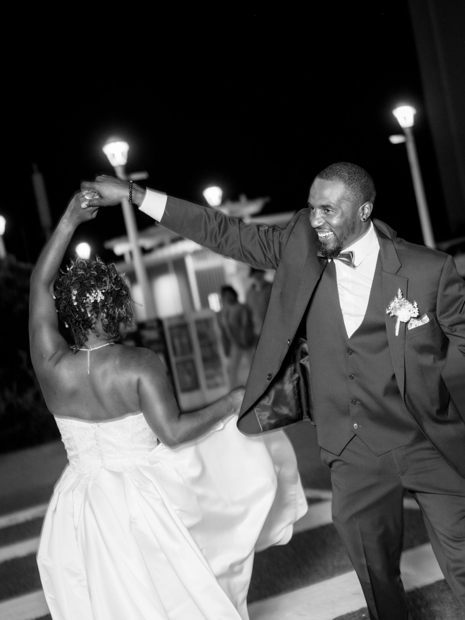 A couple dances joyfully at their nighttime wedding reception with lights in the background.