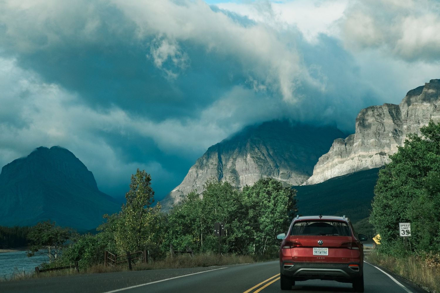 Road snaking through scenic mountain landscape under dramatic cloudy sky along Going-to-the-Sun Road in Glacier National Park.