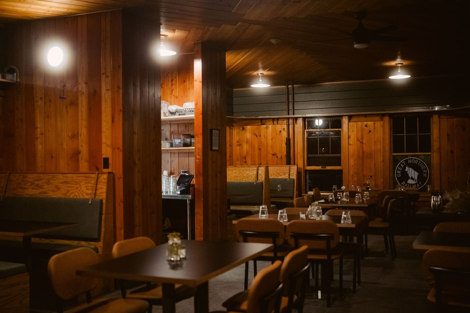 A cozy bar interior with wood paneled walls, hanging pendant lights, and rustic furniture creating a warm atmosphere.