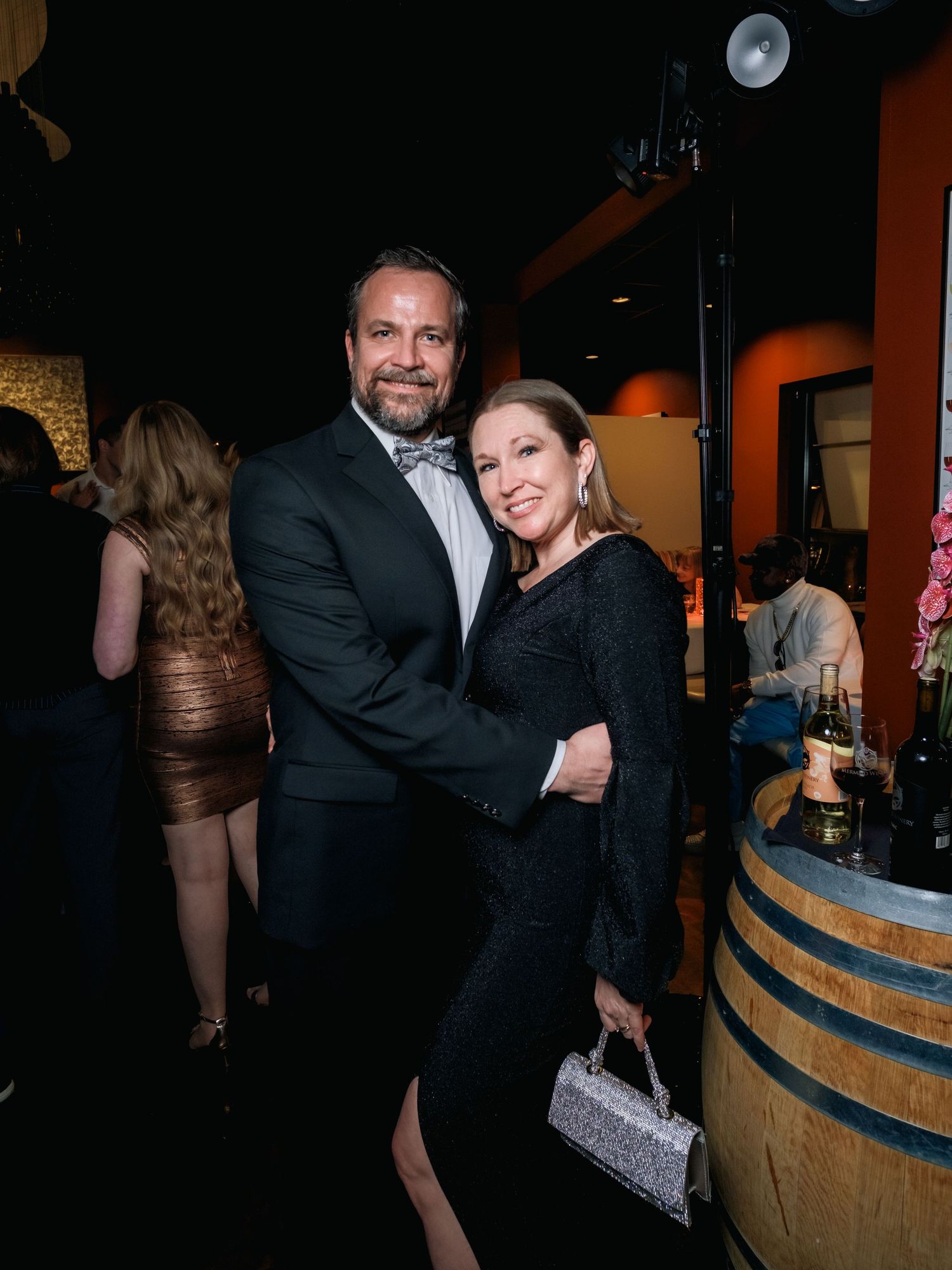 People celebrating at a formal event near wooden wine barrels in a dimly lit venue.