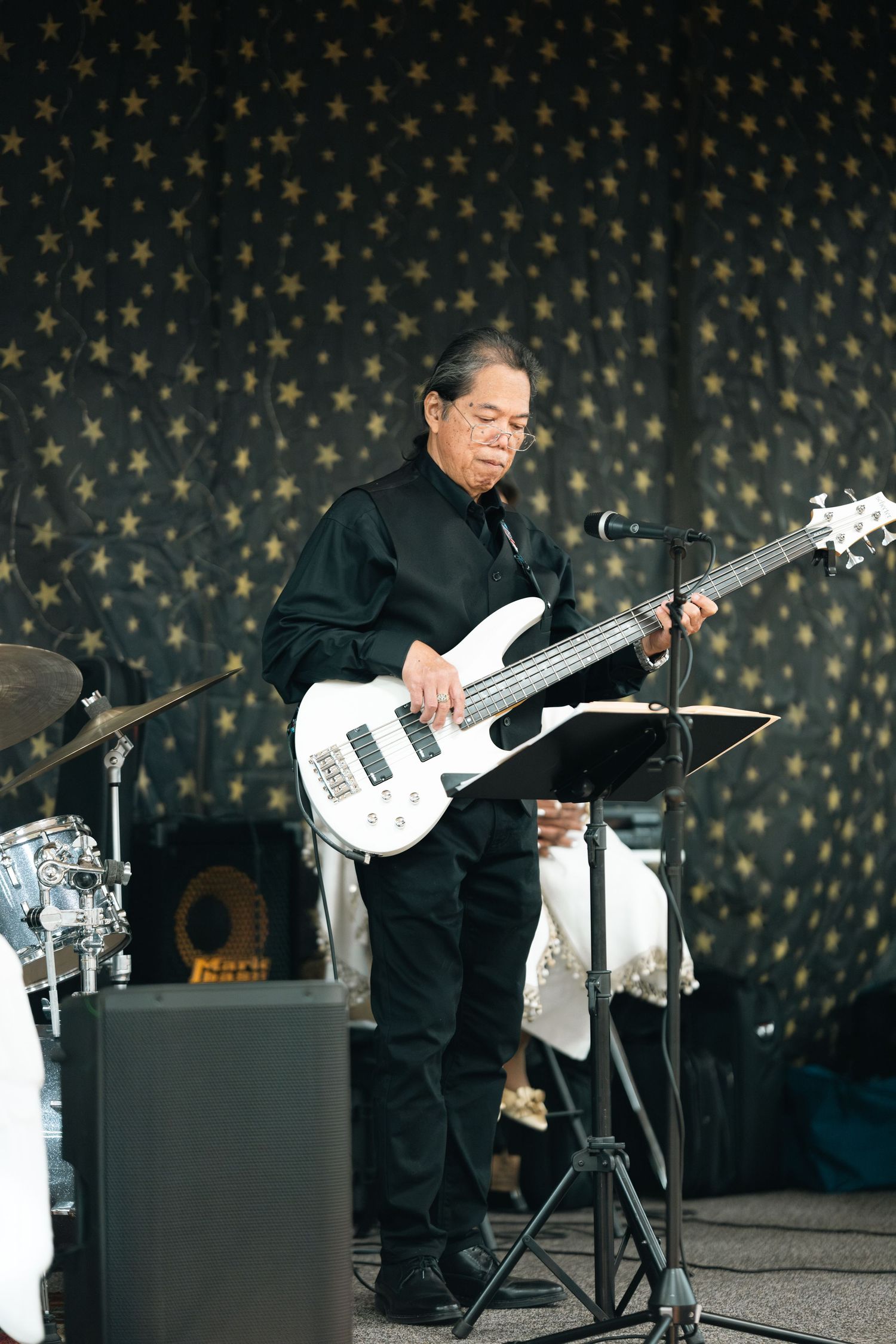 A musician in black attire performs with a white bass guitar against a star-patterned backdrop in multiple dynamic poses.