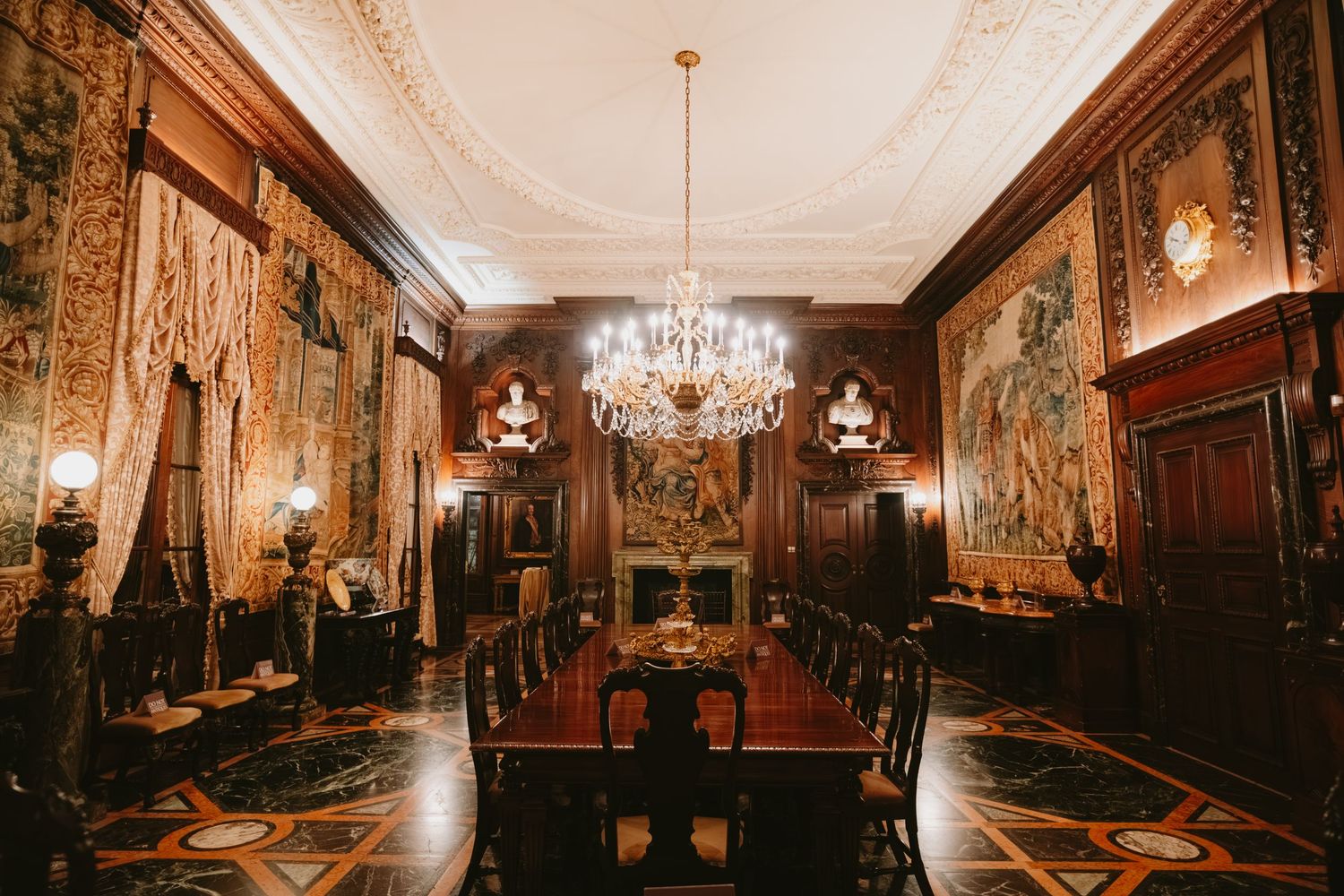Opulent palace room with ornate ceiling, crystal chandeliers, gilded walls and historic portraits in a grand gallery setting.