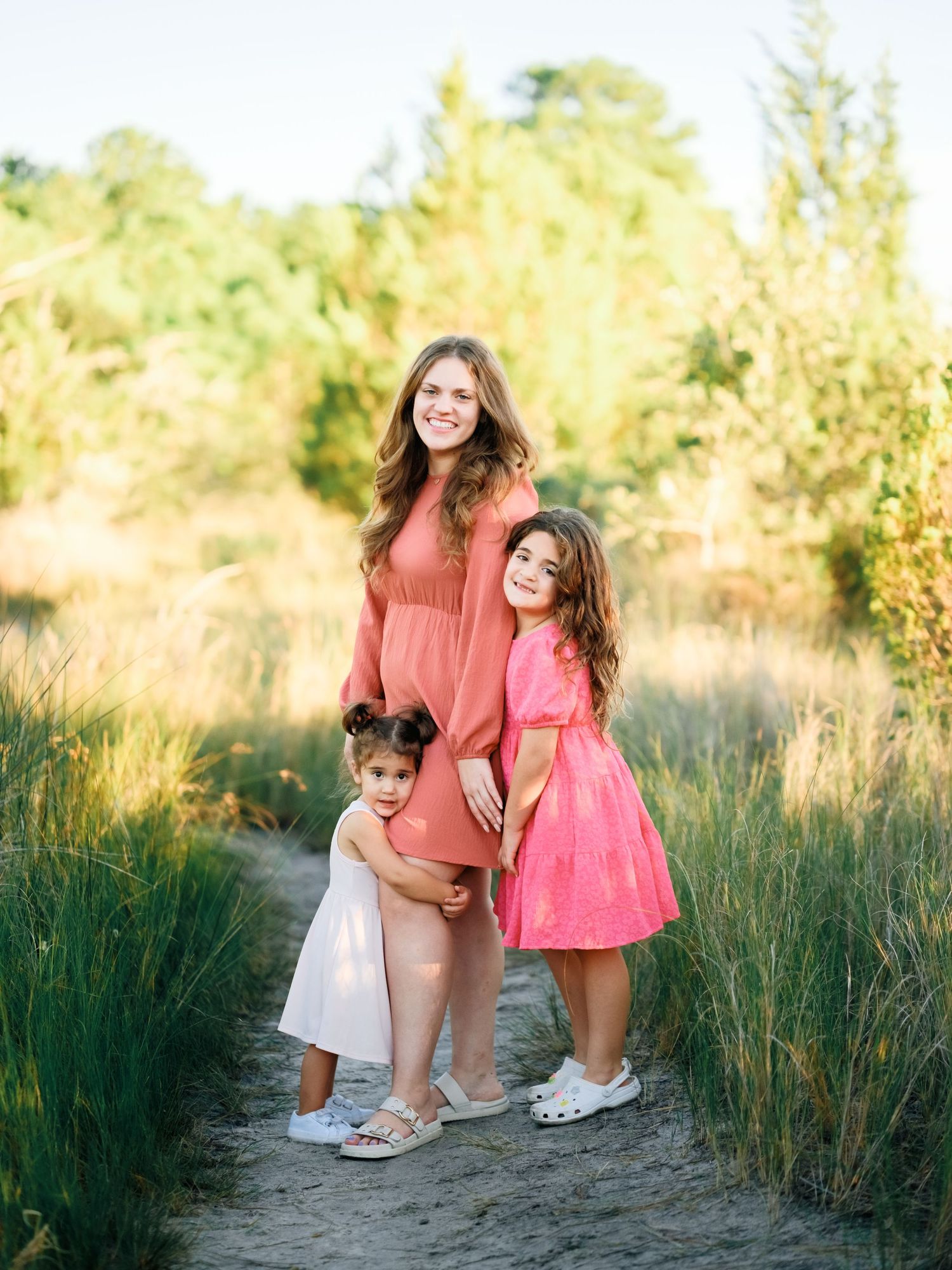 Family enjoying a tender moment together on a nature path surrounded by tall golden grasses at sunset.
