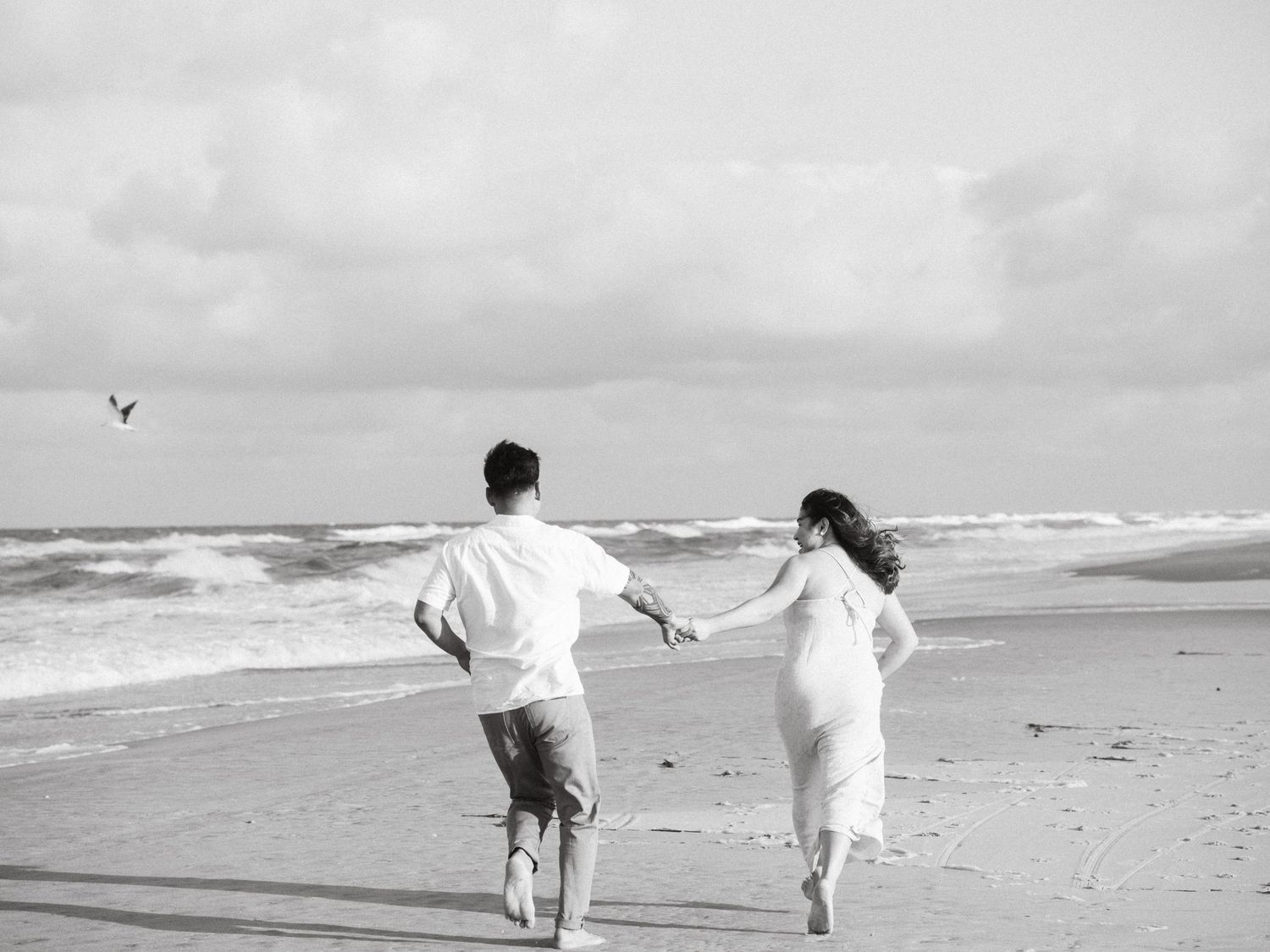 Artistic black and white series of five photos showing a couple walking along a beach with waves in the background.