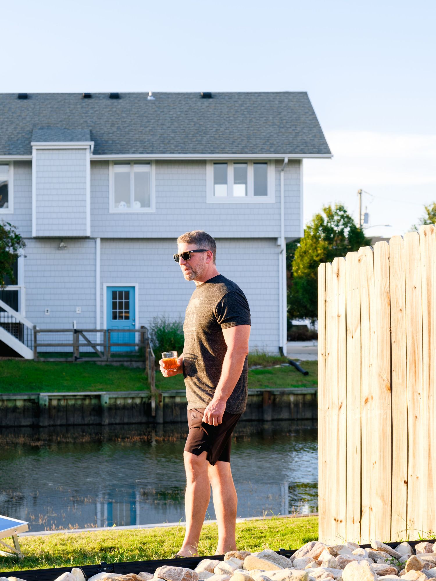 A person in workout clothes relaxes near a wooden fence and calm water at sunset.