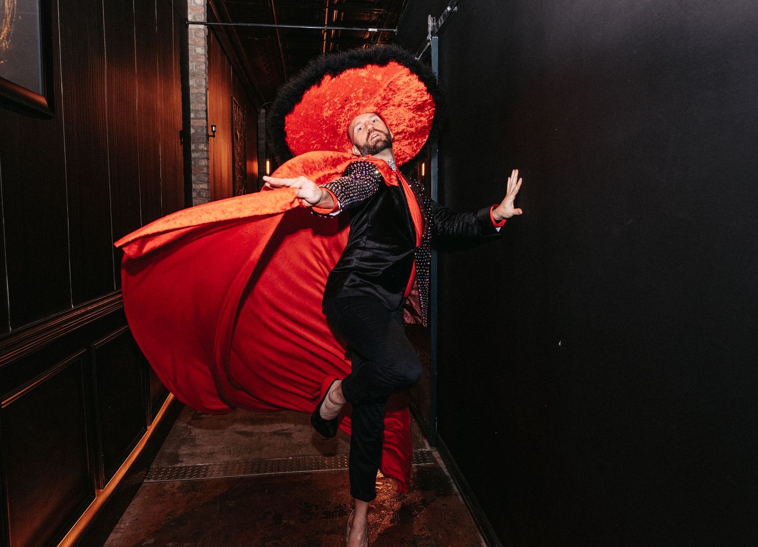 Person with bright red hair and red dress spins dramatically in a dark hallway.
