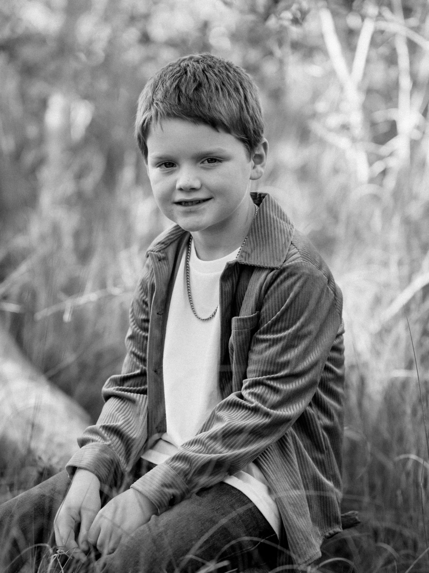 Black and white portrait series of a young child sitting outdoors in a casual jacket and white shirt.