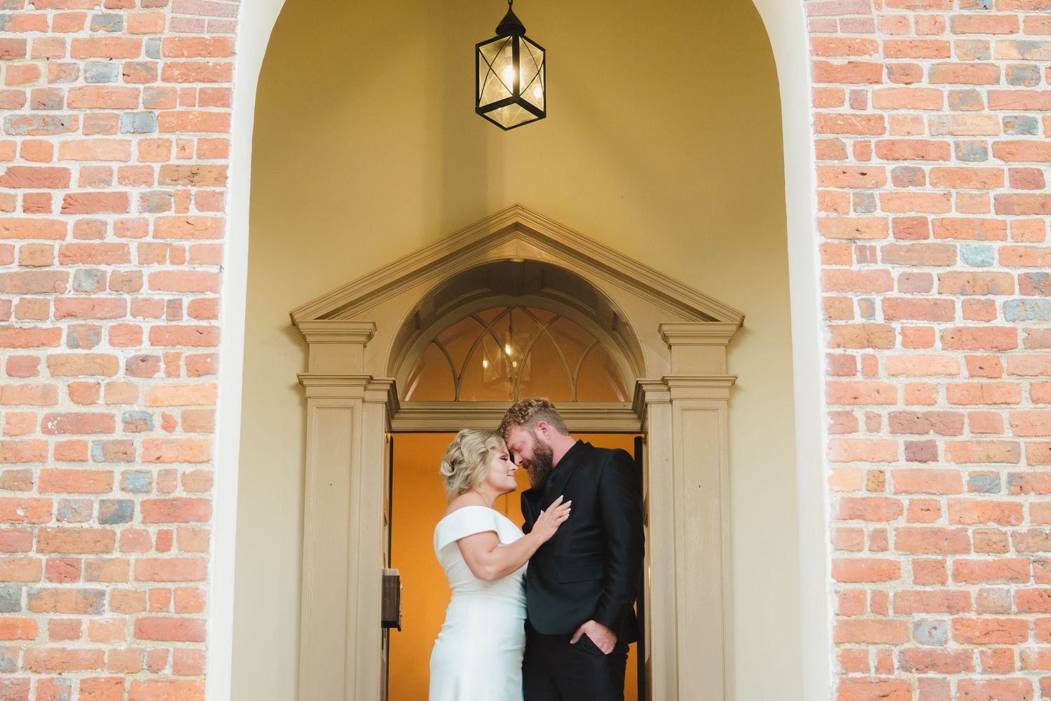 A series of bright arched doorways in a red brick church building with traditional lantern lighting fixtures.