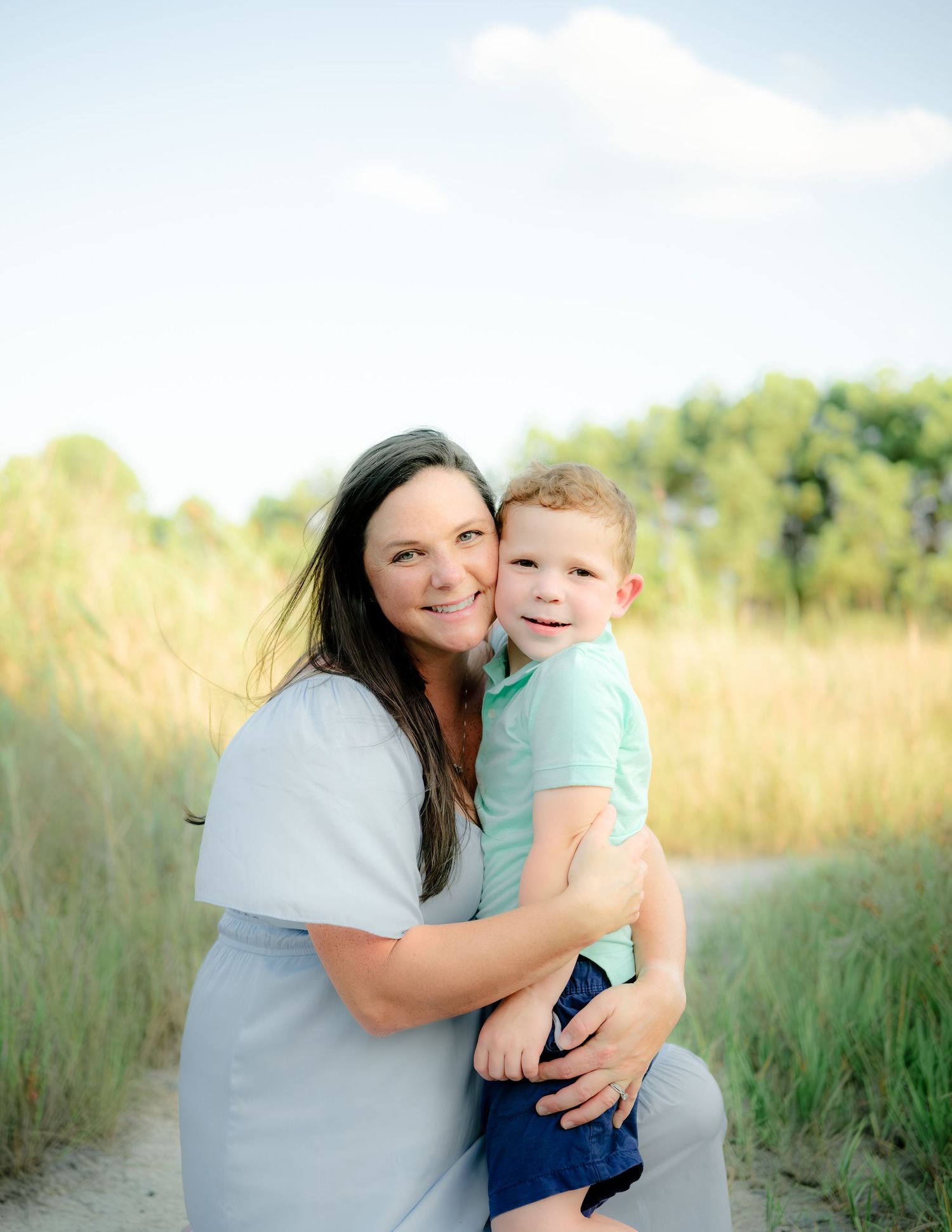 A parent and child share a joyful moment together in a sunlit field of tall summer grass.