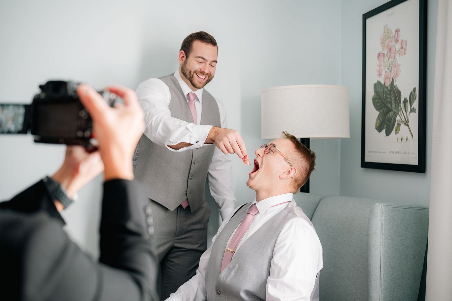 A photographer captures a candid moment between two men in formalwear laughing during a photography session.