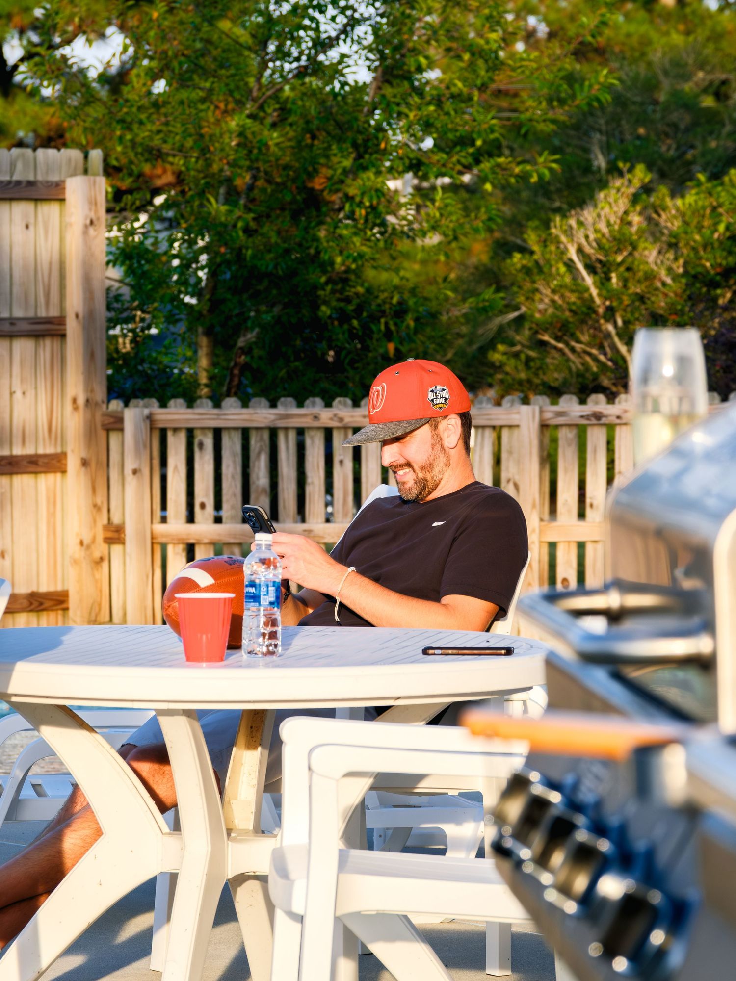 Person wearing an orange baseball cap sitting at outdoor picnic table on sunny afternoon.