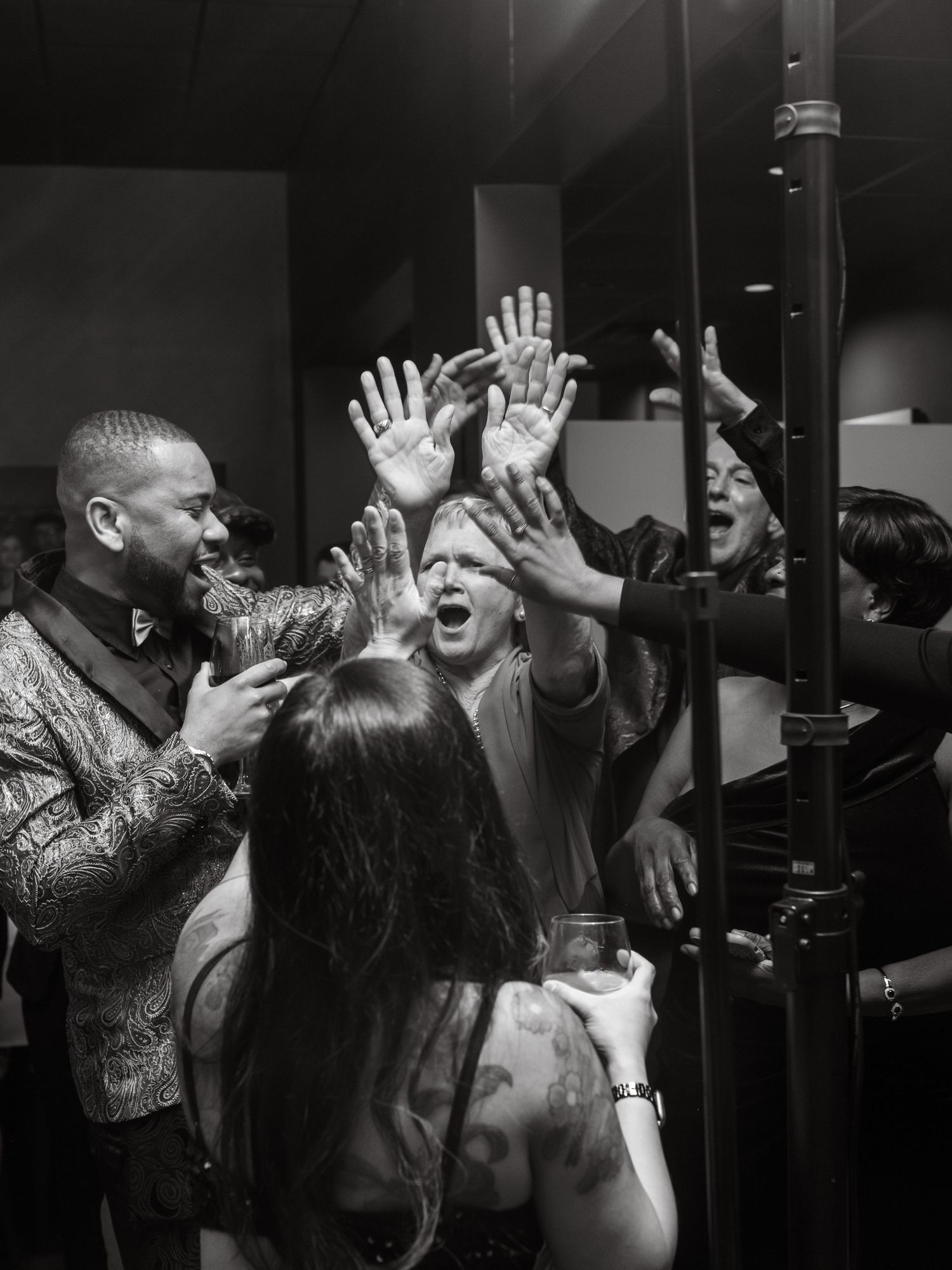 Black and white photo of a passionate crowd at a concert with raised hands reaching up into the air.