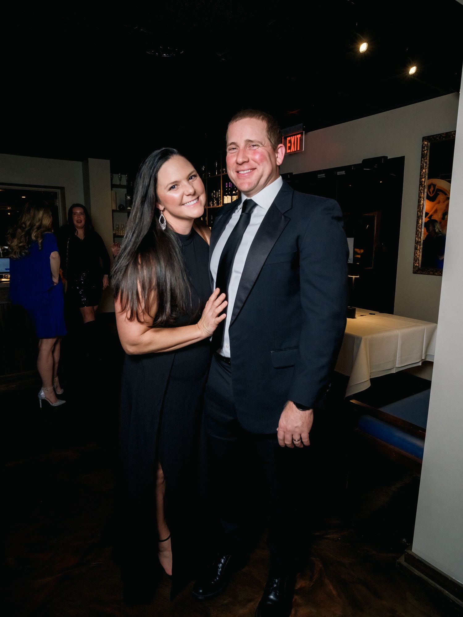 A couple dressed in formal attire pose together at an elegant indoor event space.