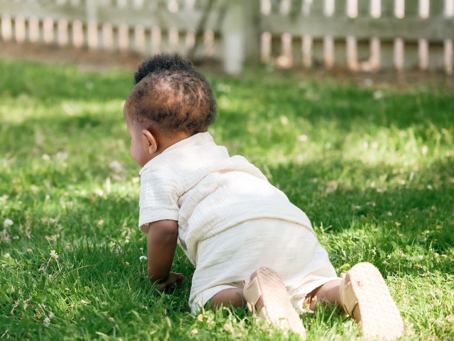 Baby in white clothing crawls through sunny green grass on a summer day while being photographed in motion.