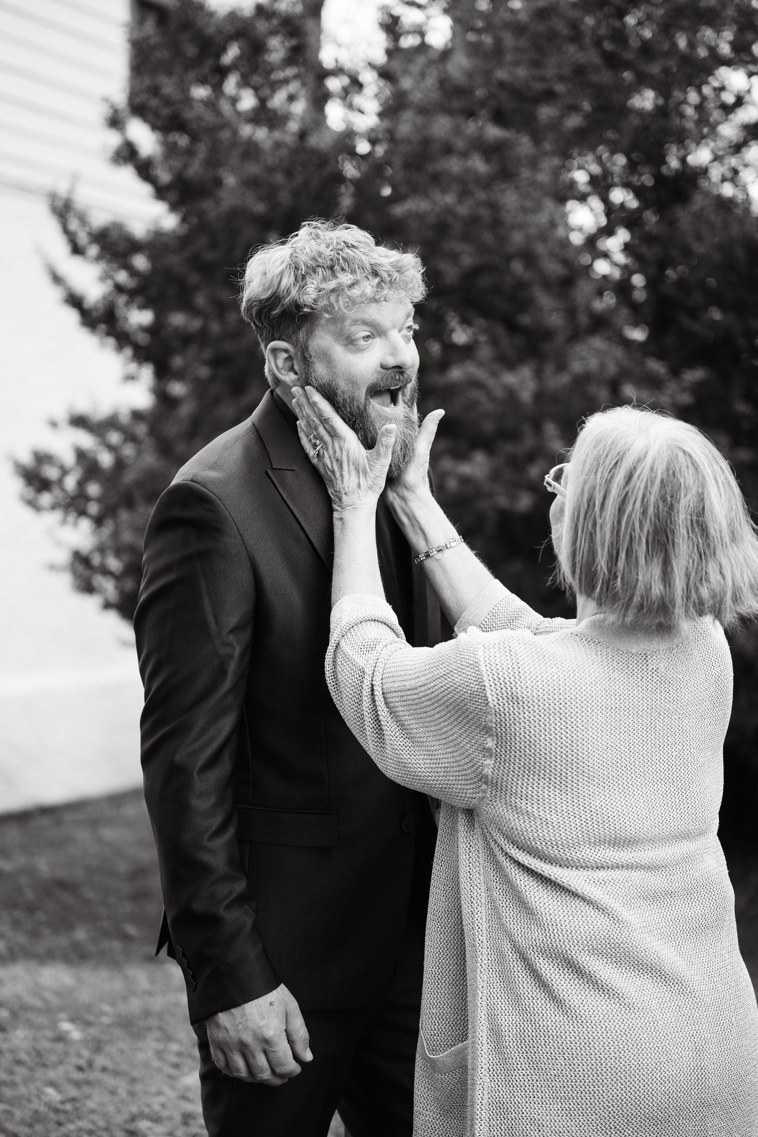 Black and white candid photo showing an emotional moment between a mother and son at an outdoor event.