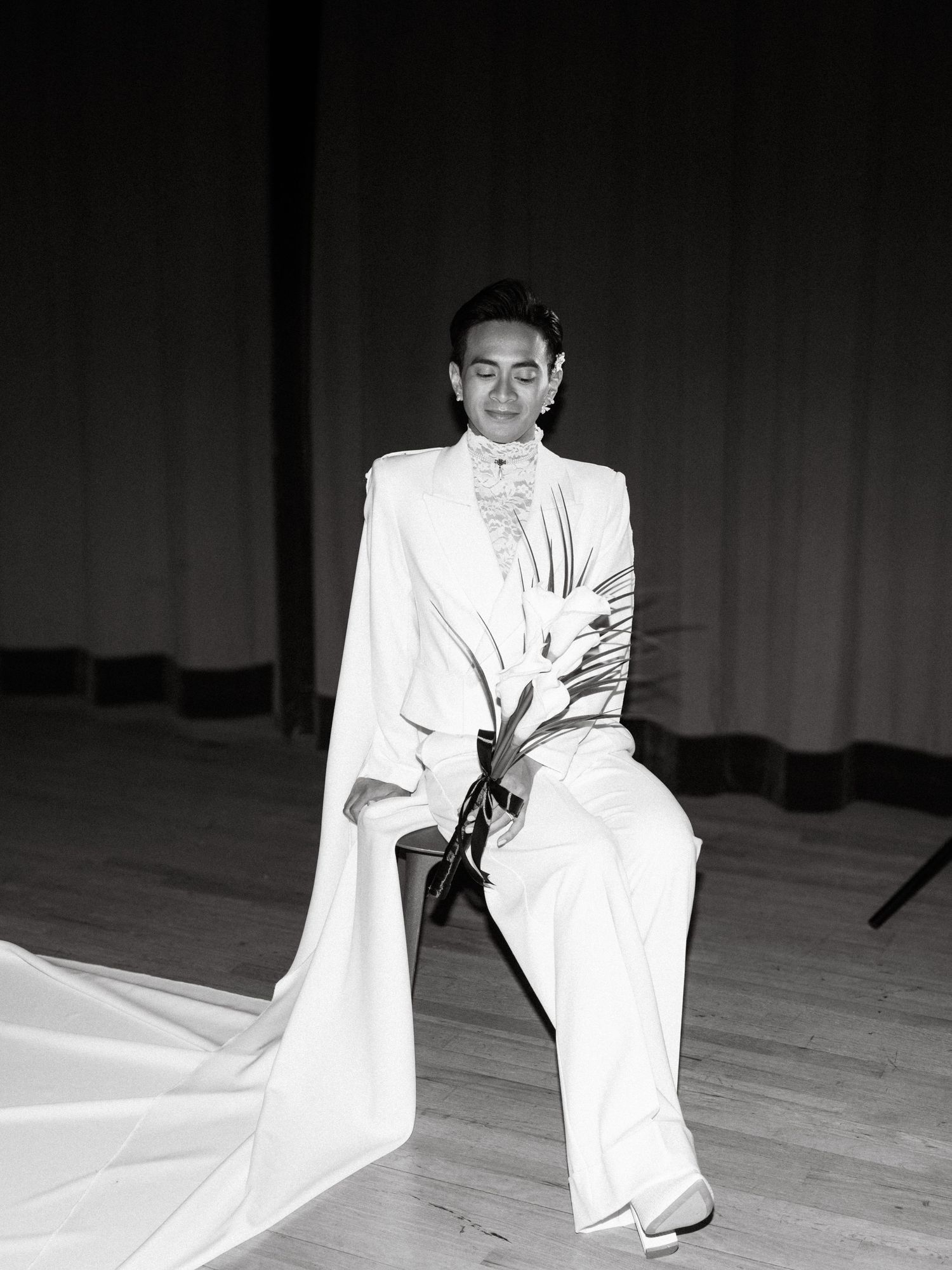 A performer in an elegant white ensemble strikes a dramatic pose on stage in a black and white photograph.