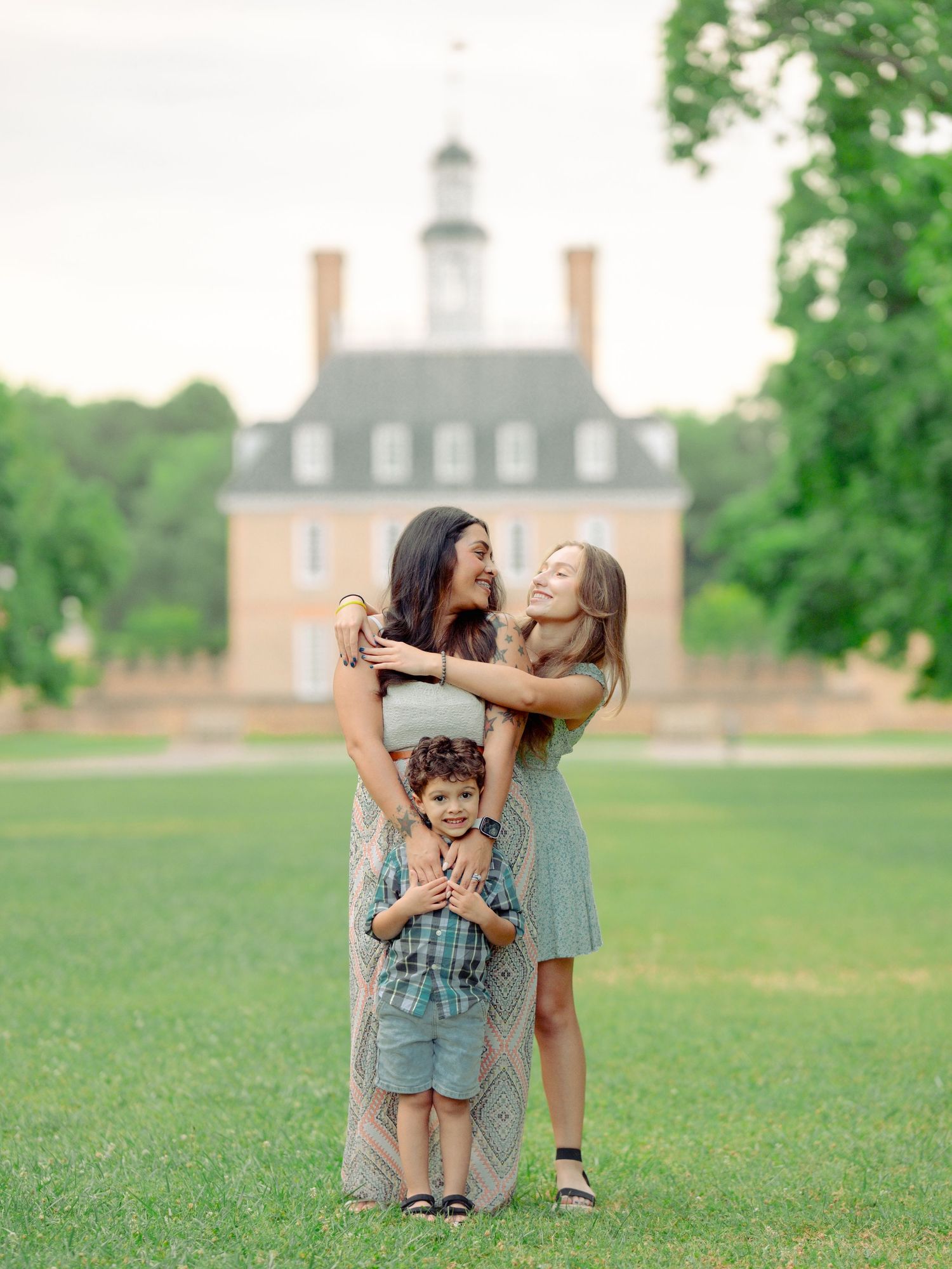 A family shares joyful laughter together on a green lawn with the historic Governor's Palace at Colonial Williamsburg in the background.