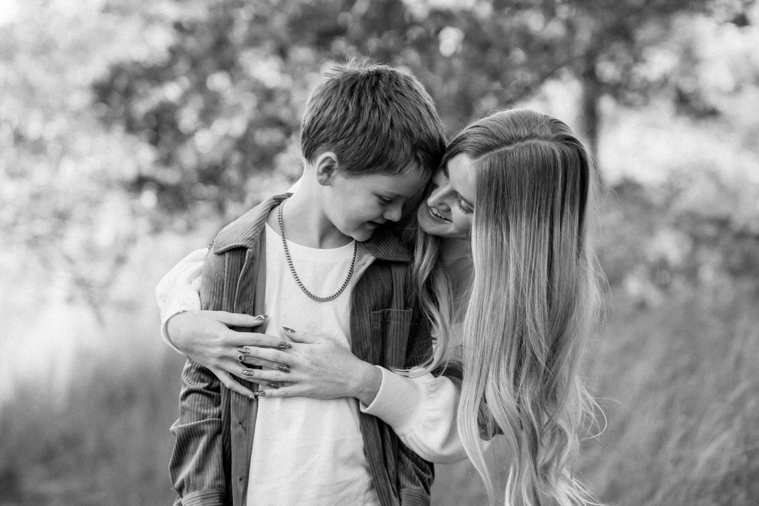 A tender black and white moment between two young people embracing outdoors with soft natural lighting in the background.