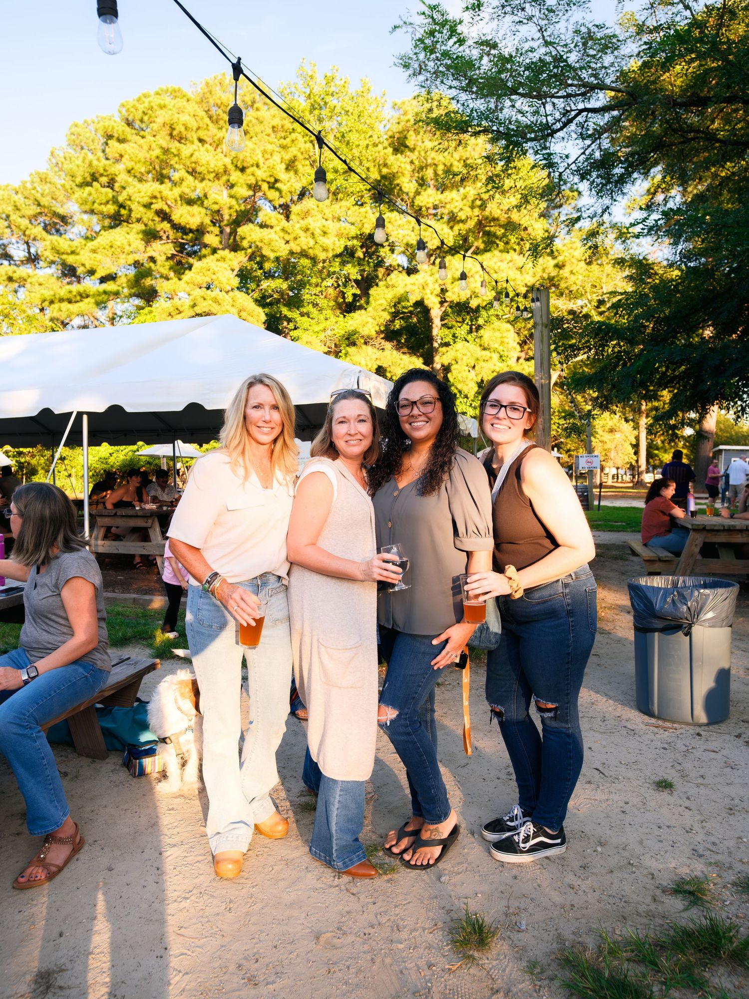 Group of friends celebrating at an outdoor party with string lights and trees glowing in golden sunlight.