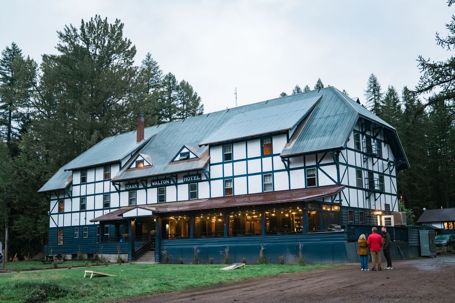 Historic Tudor-style lodge with black and white timber framing stands illuminated at dusk against a pine forest backdrop.