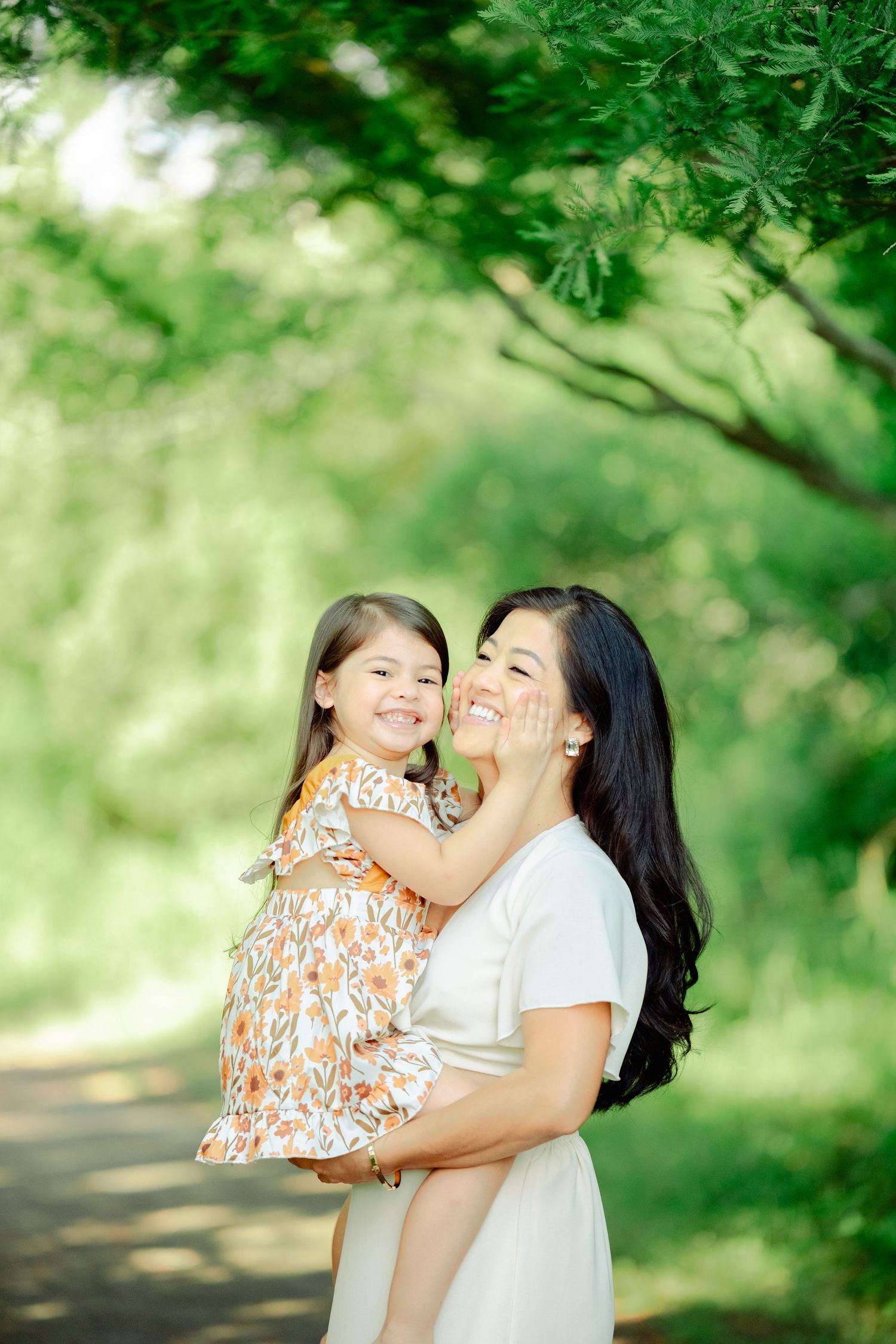 A tender outdoor portrait of two figures embracing on a sunlit path surrounded by lush green foliage.