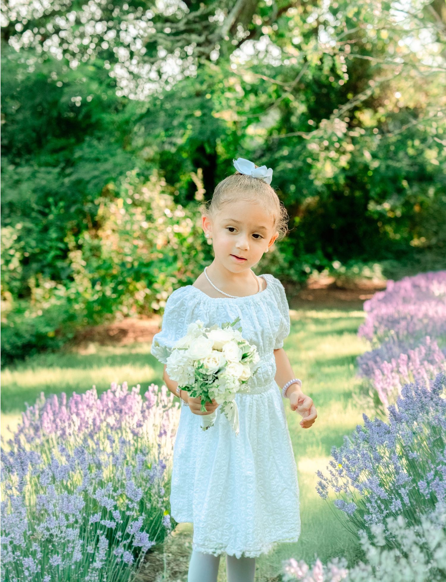 A small figure in a light blue dress stands in a garden filled with blooming lavender flowers and lush greenery.