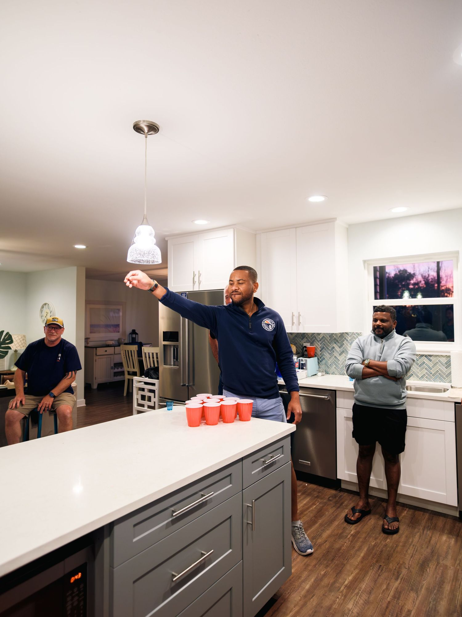 A sequential progression shows people lining up red plastic cups on a white kitchen countertop during a game setup.