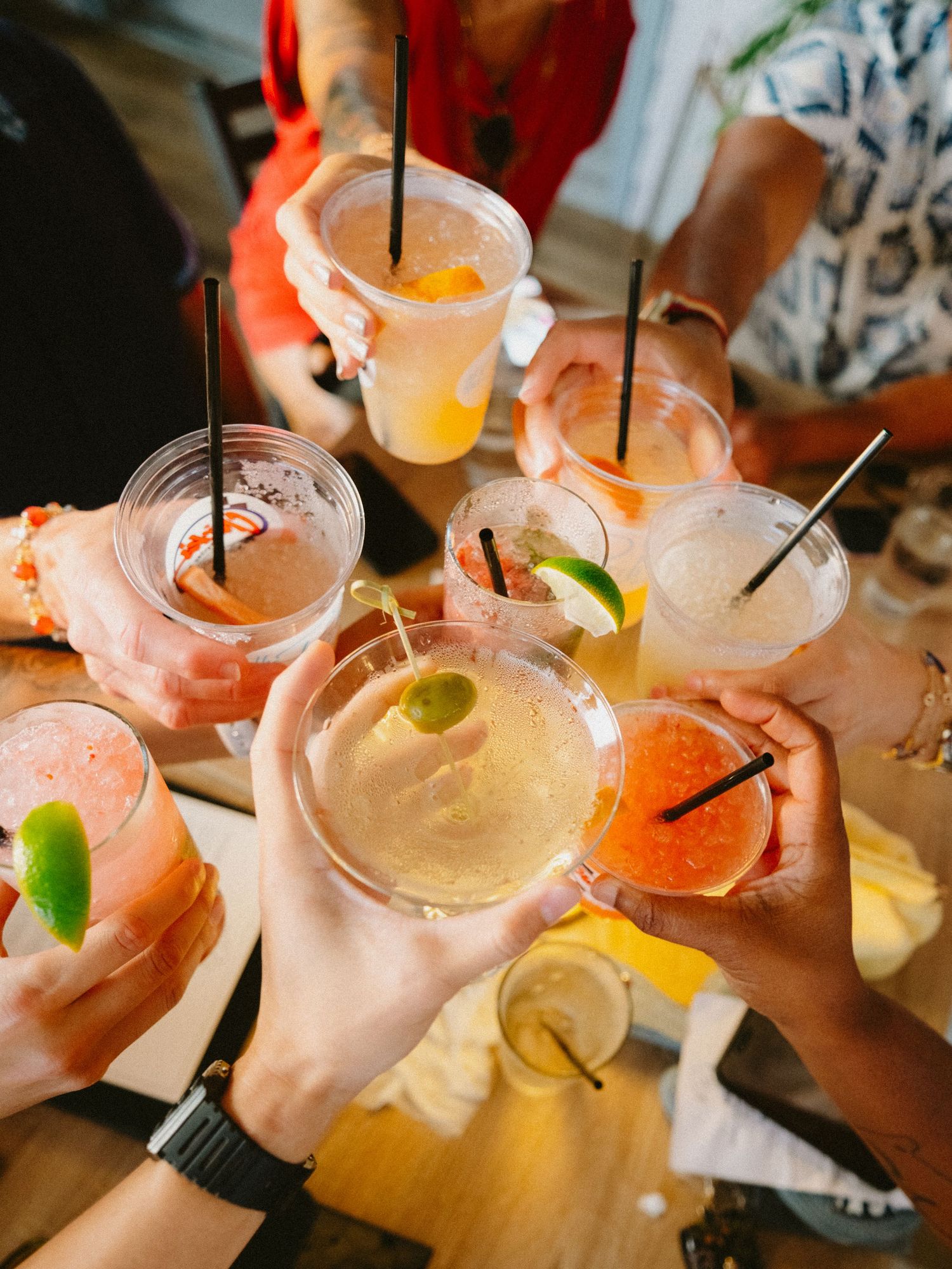 Friends clink colorful tropical cocktails in mason jars garnished with fresh fruit at a summer party gathering.