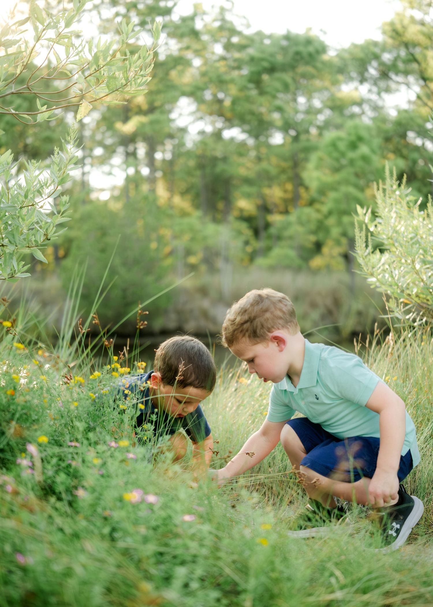 Two children explore and pick flowers together in a lush garden setting on a sunny day.