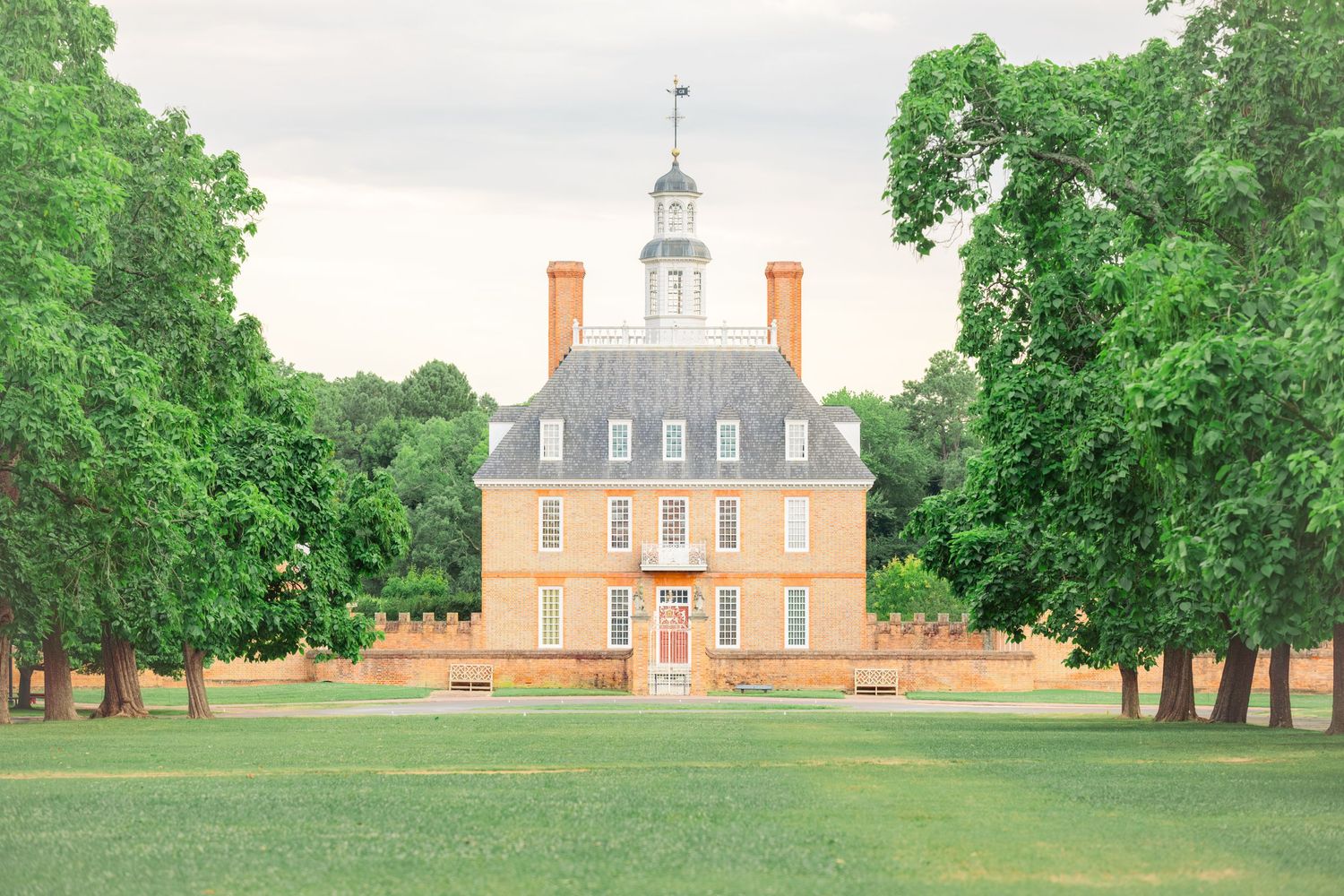 Georgian-style Governor's Palace with peach-colored exterior and white trim stands majestically amid green lawns in Colonial Williamsburg.