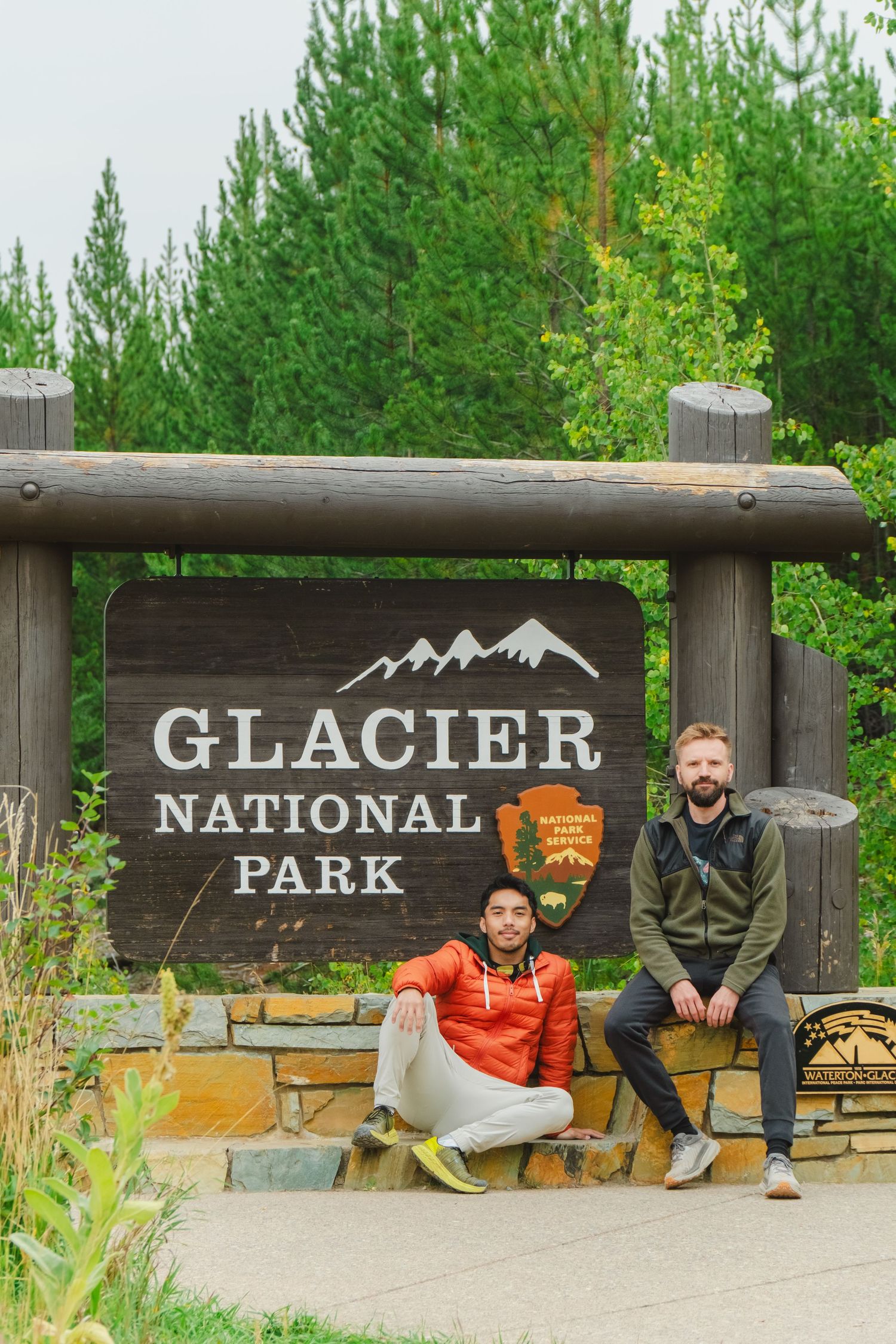 Wooden entrance sign for Glacier National Park with National Park Service logo and mountain peaks carved into dark wood.