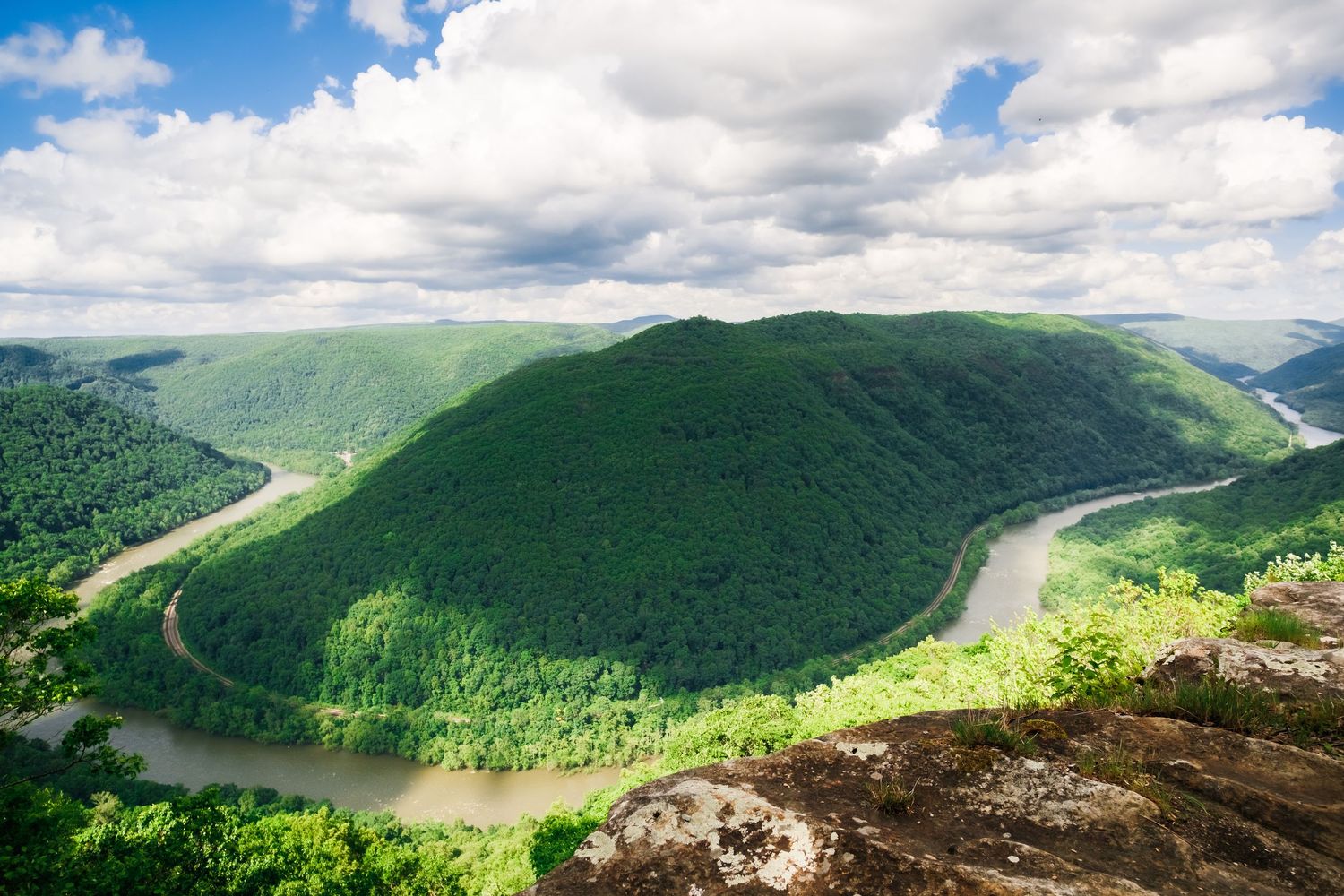 Panoramic view of lush green mountains and a winding river valley under dramatic cloudy skies.