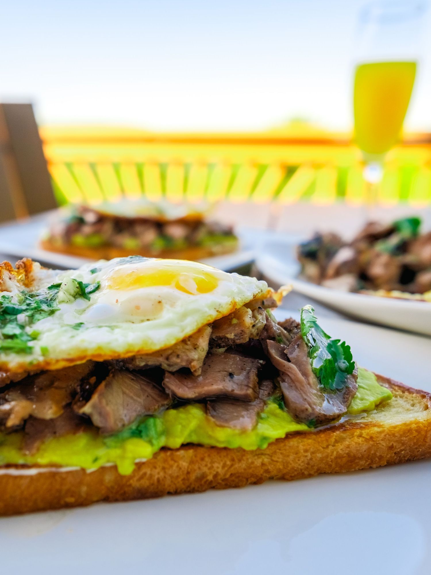 Open-faced sandwich with sliced steak, lettuce, and sunny side up egg on toasted bread.