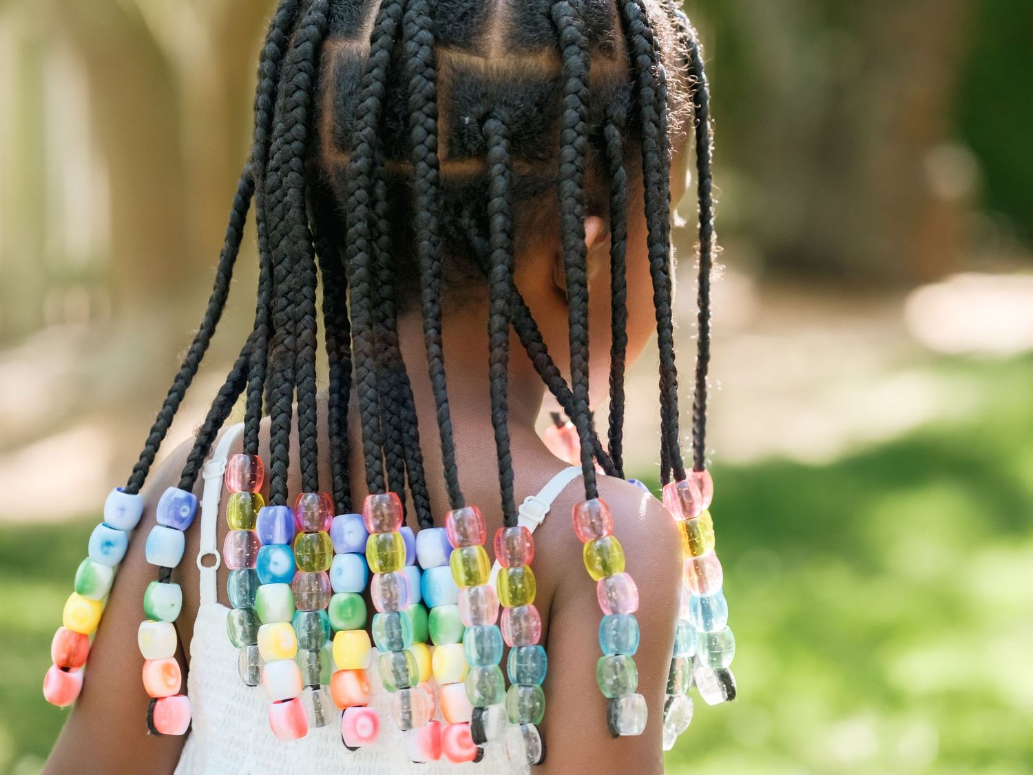 Colorful beaded hair braids with cornrows decorated with pastel plastic beads hanging down outdoors.