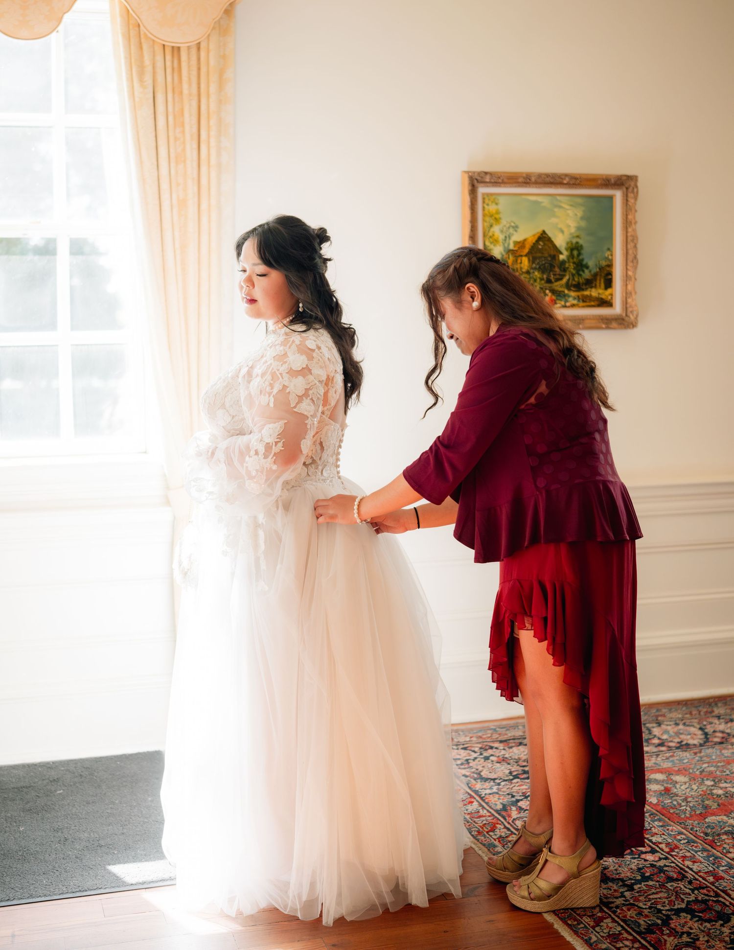 Wedding preparation scene with a person helping to button up a delicate white lace and tulle bridal gown.