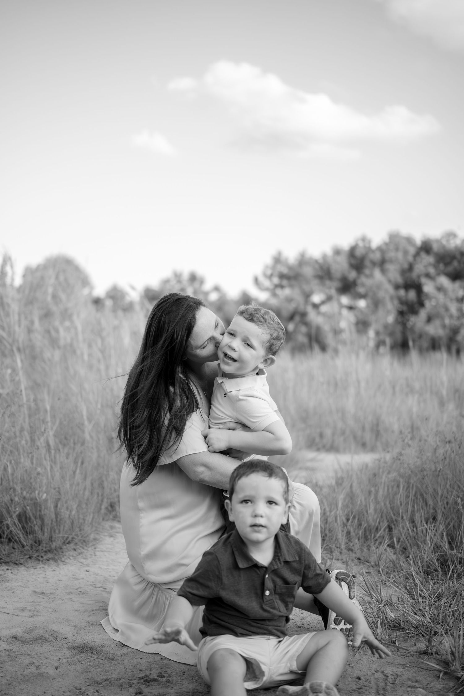 A candid black and white sequence shows a loving family moment together in a grassy outdoor field.