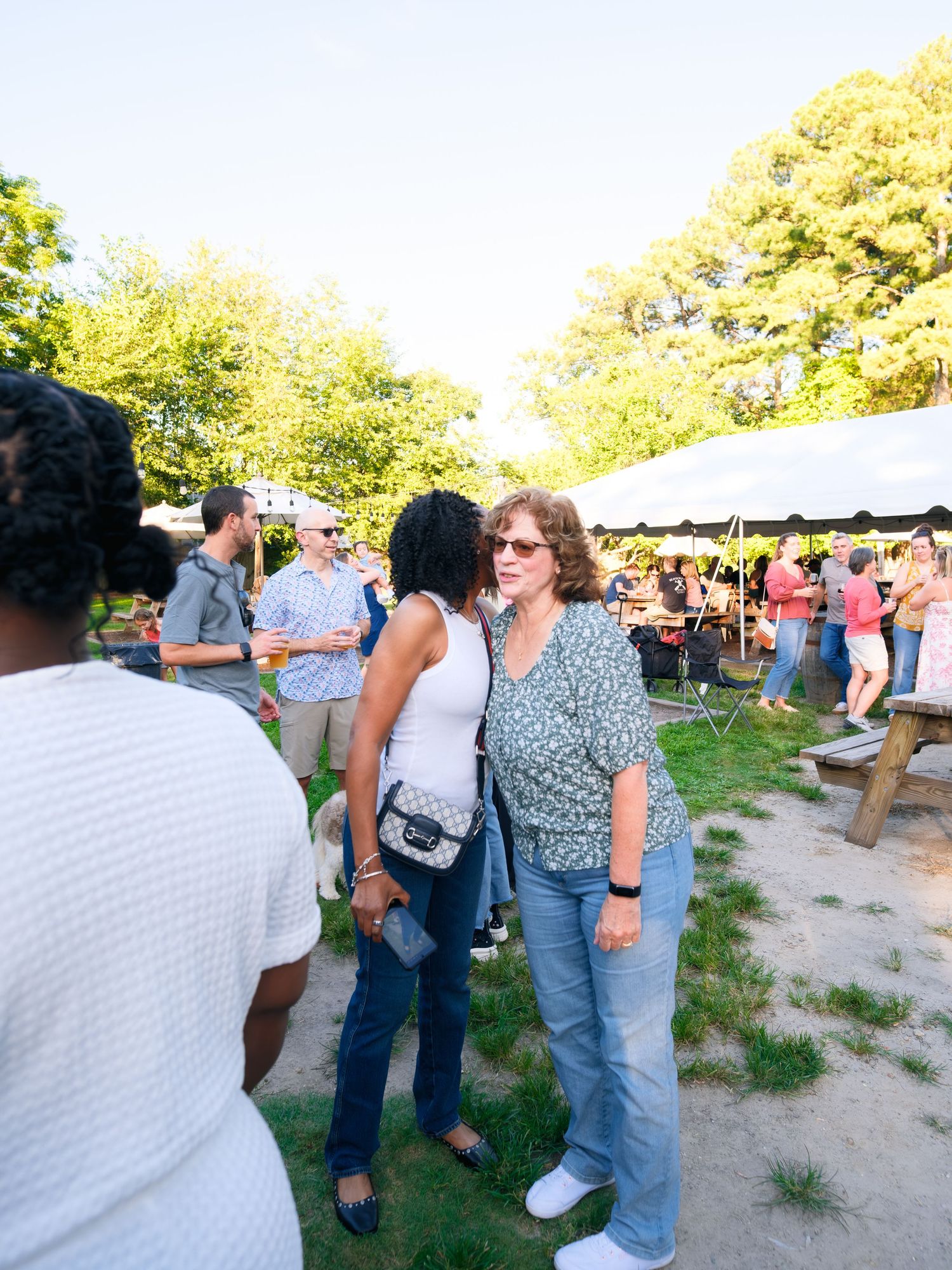 Groups of people gather outdoors at a casual summer event in a grassy area during golden hour.
