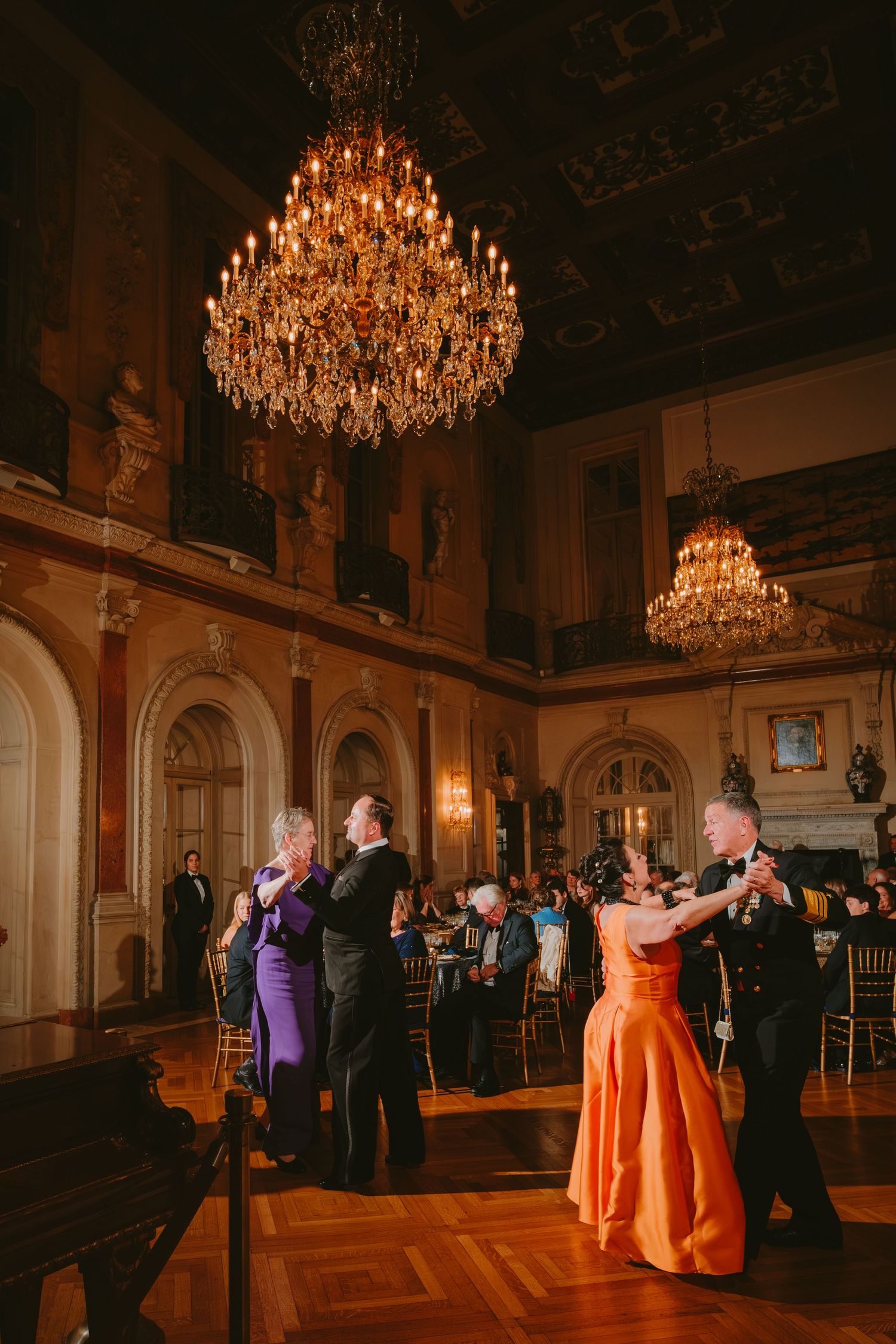 Elegant ballroom dance scene with crystal chandeliers and couples dancing in formal attire at an ornate venue.