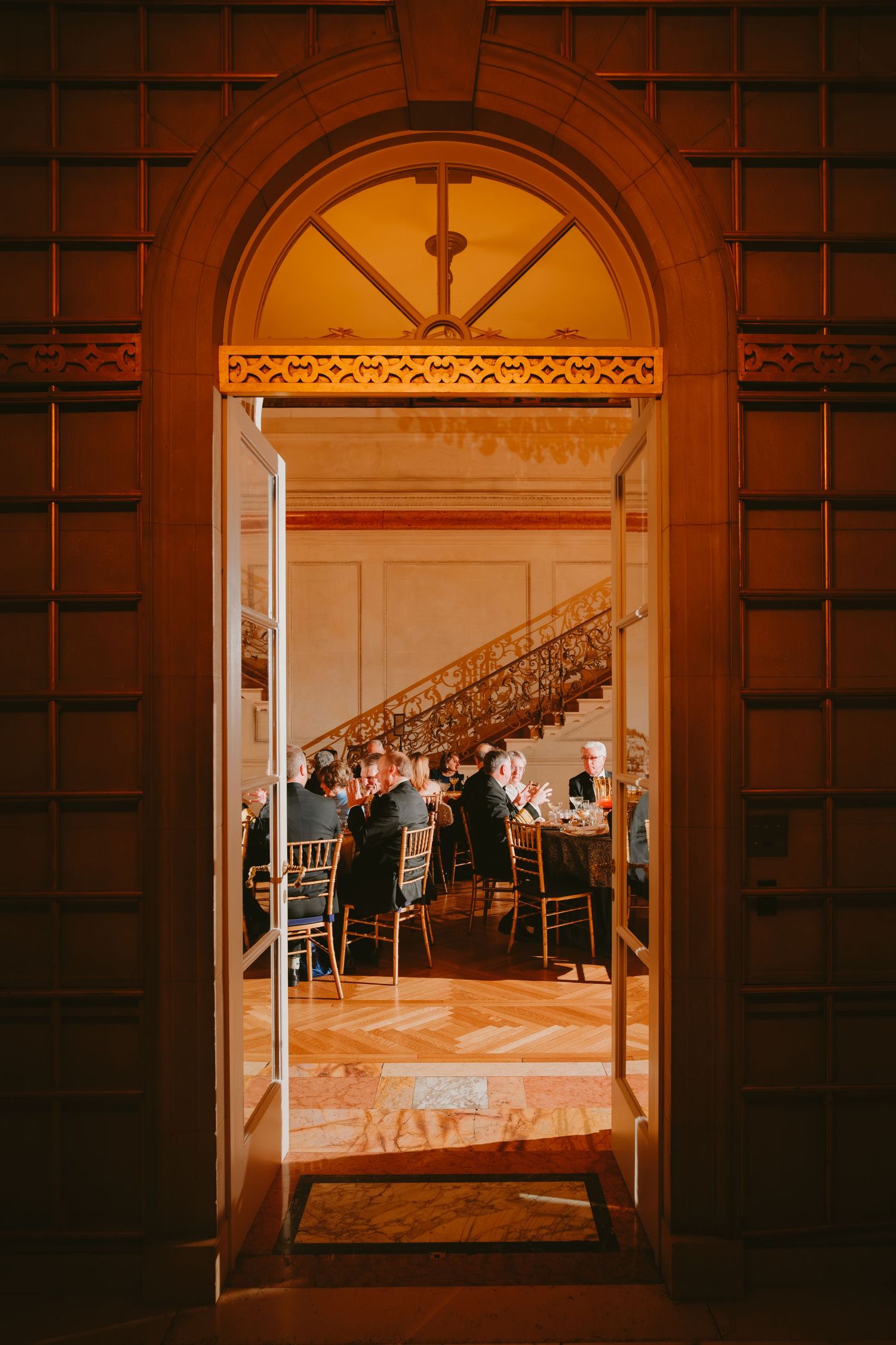 View through an ornate archway into an elegant dining room with guests seated at tables for a formal event.