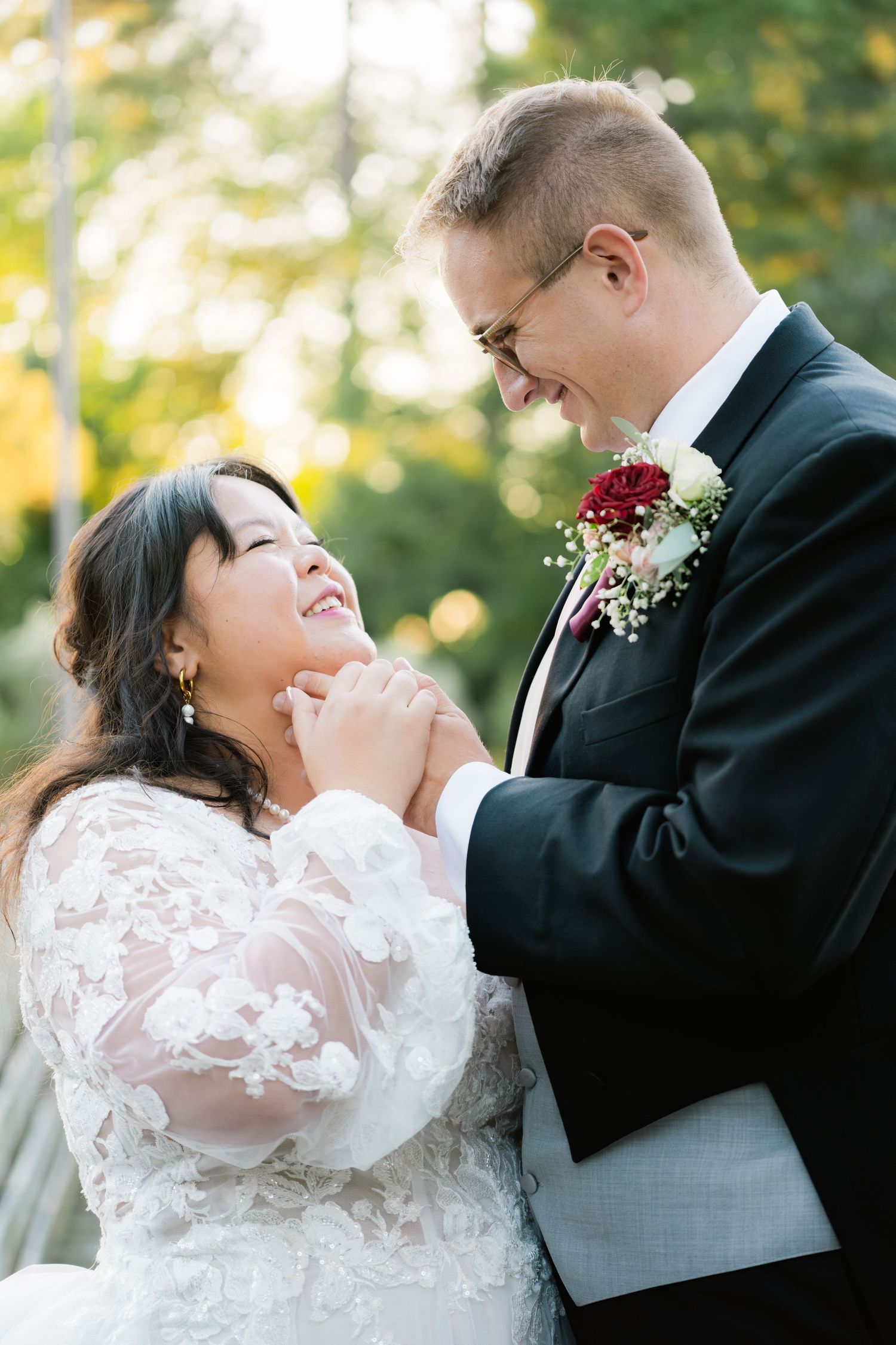A happy couple shares a loving moment outdoors on their wedding day wearing formal attire with autumn colors in background.