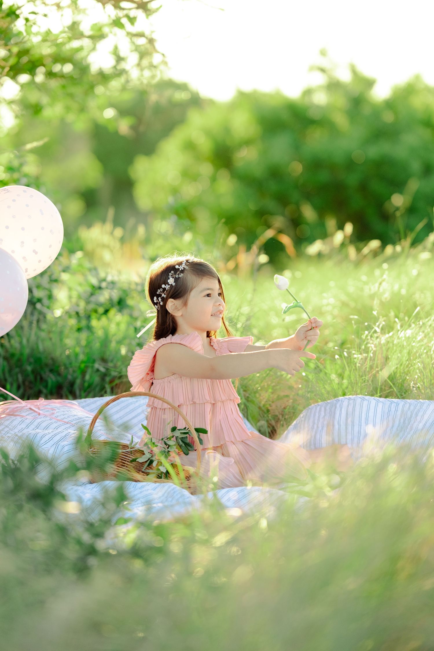 Outdoor spring picnic scene with balloons and blanket on grass in soft natural lighting.