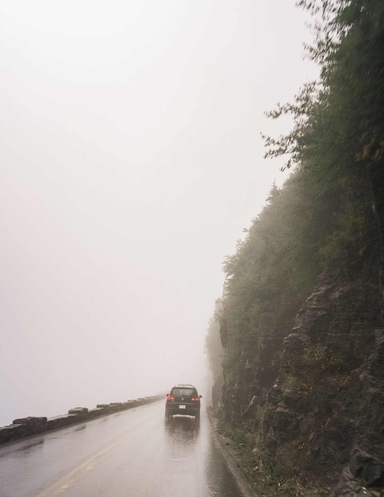 A foggy mountainside road curves through dense forest in misty conditions with low visibility.