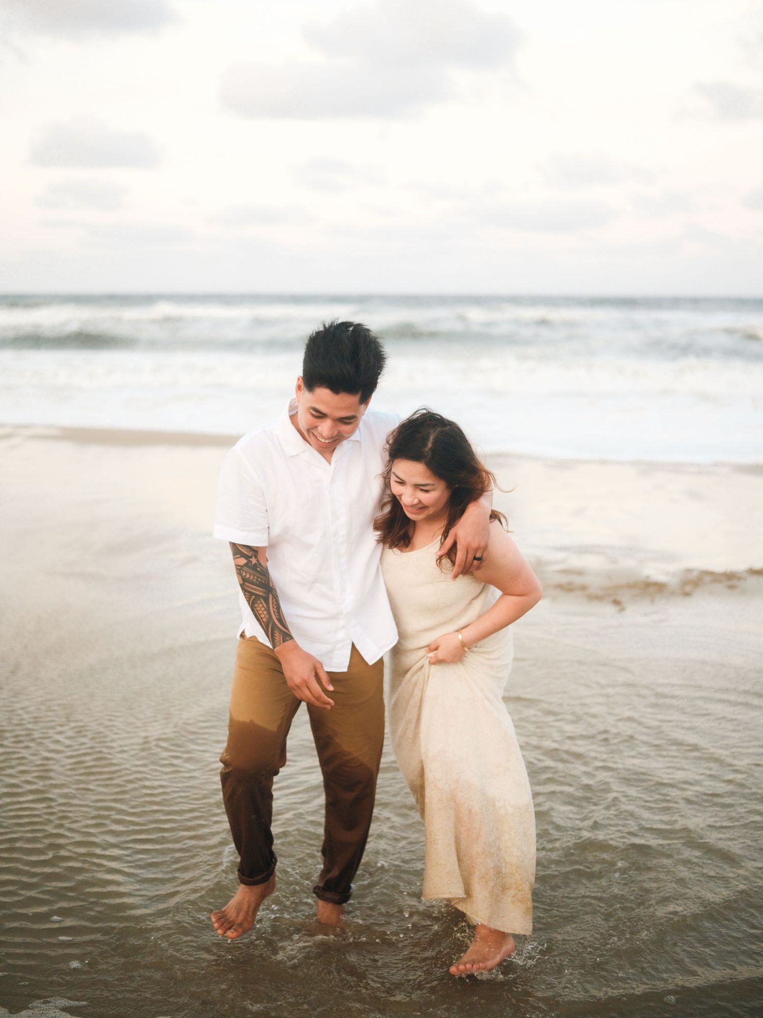 Couple playing in shallow ocean water at the beach during sunset.