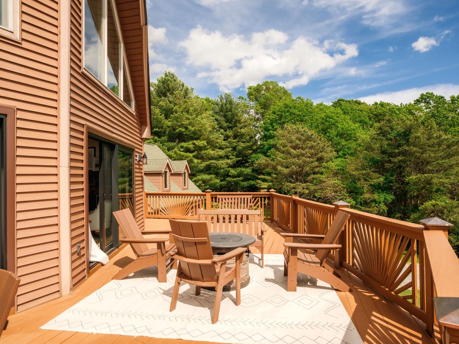 Large wooden deck with Adirondack chairs overlooking a wooded area on a sunny day with blue skies.