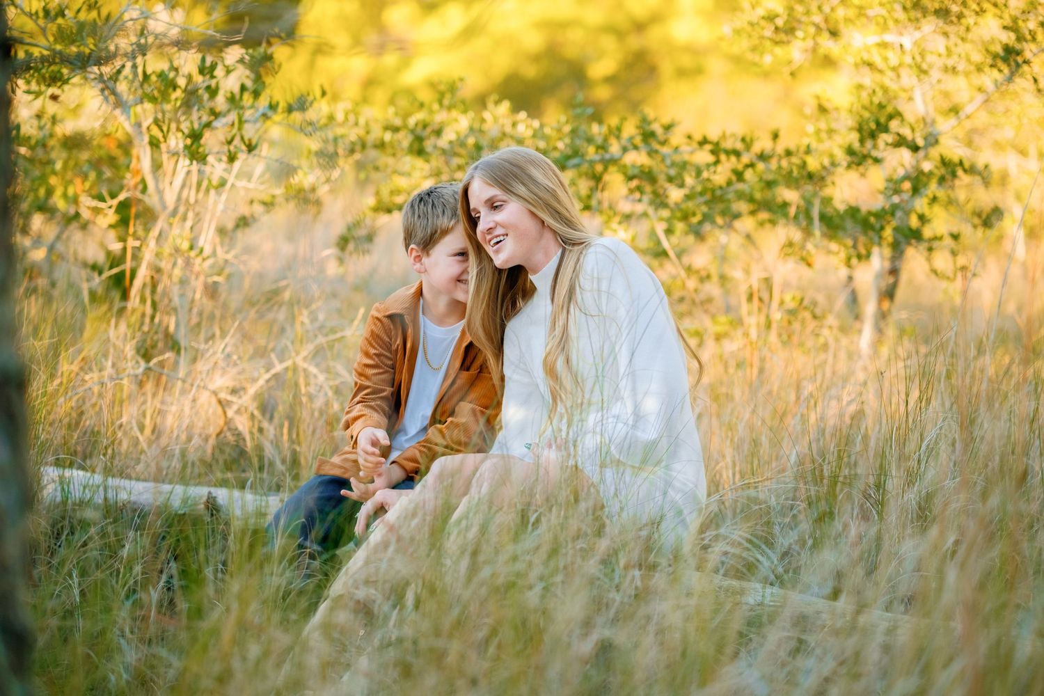 A couple shares intimate moments in a sunlit meadow during golden hour as autumn foliage glows in the background.