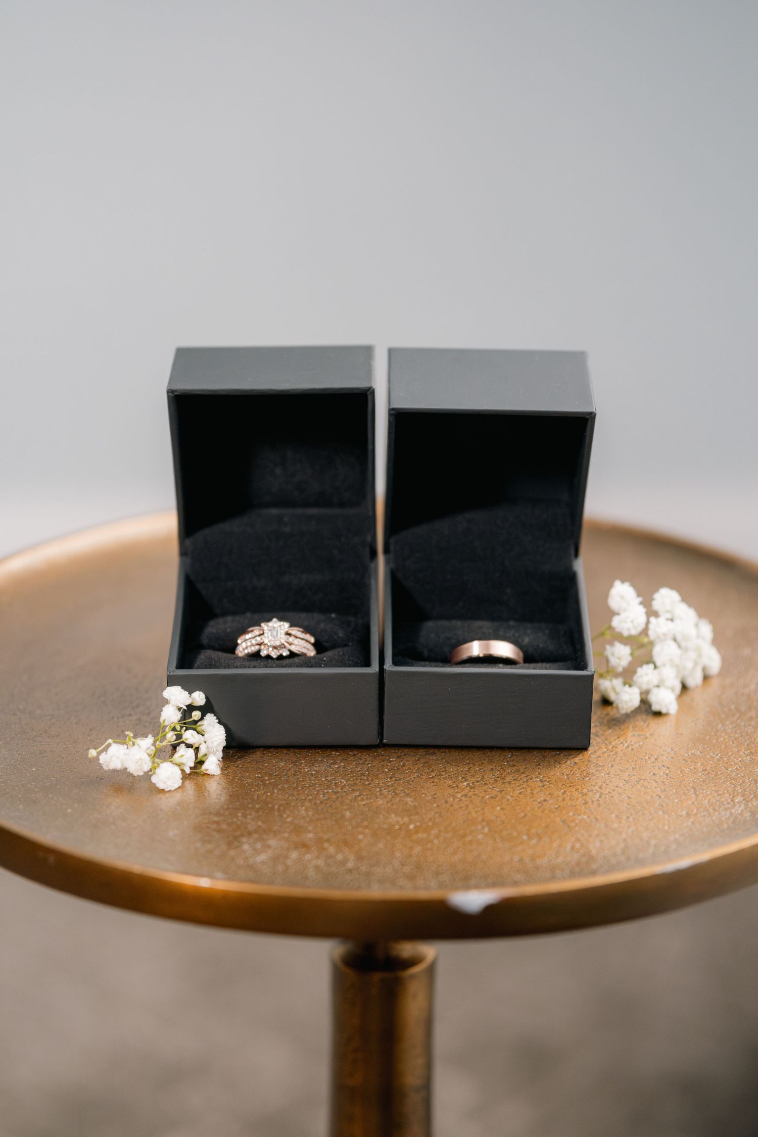 Two elegant engagement rings nestled in black jewelry boxes sit atop a round copper-colored table with scattered popcorn.
