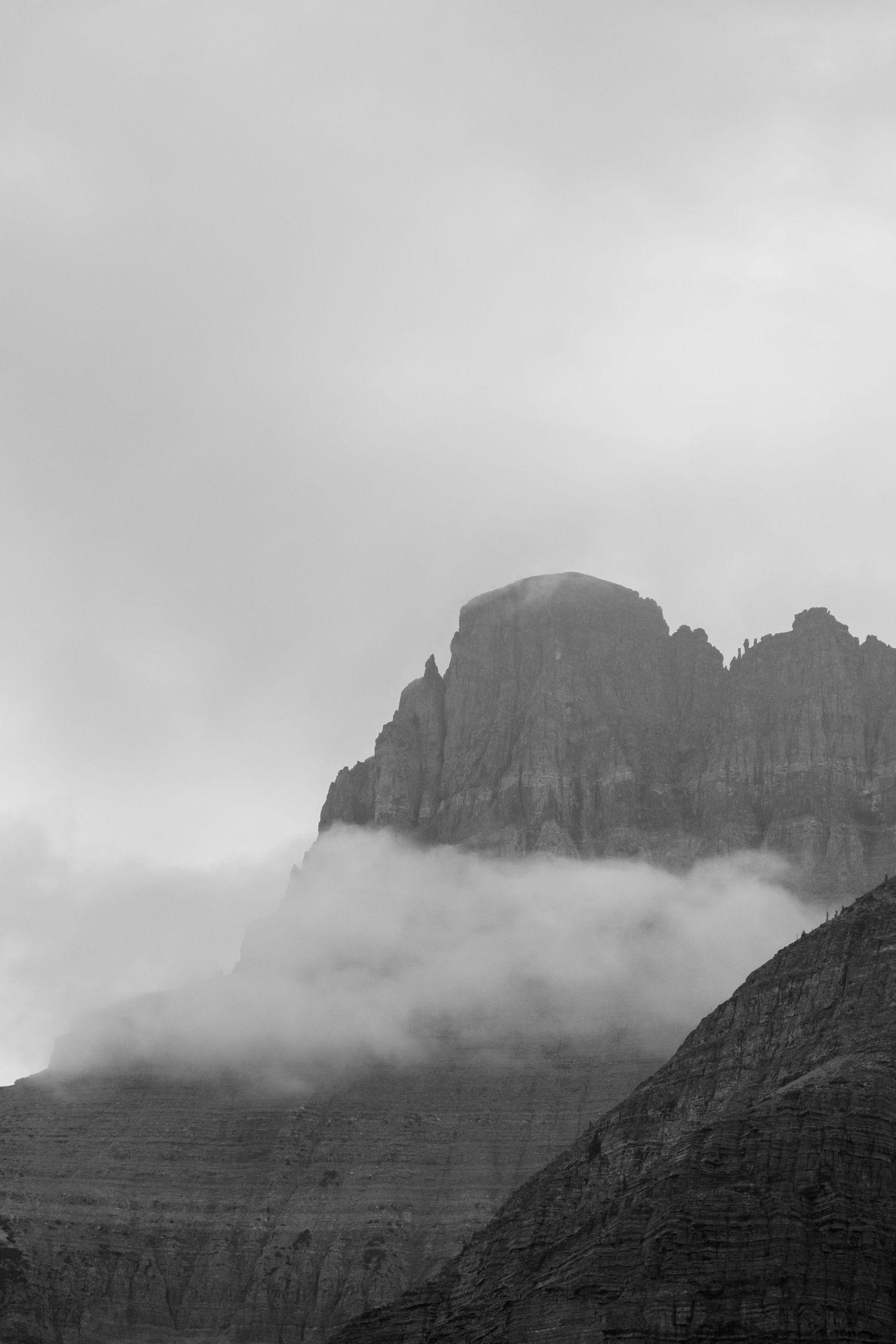 Dramatic black and white mountain peak partially shrouded in misty clouds against a moody sky.