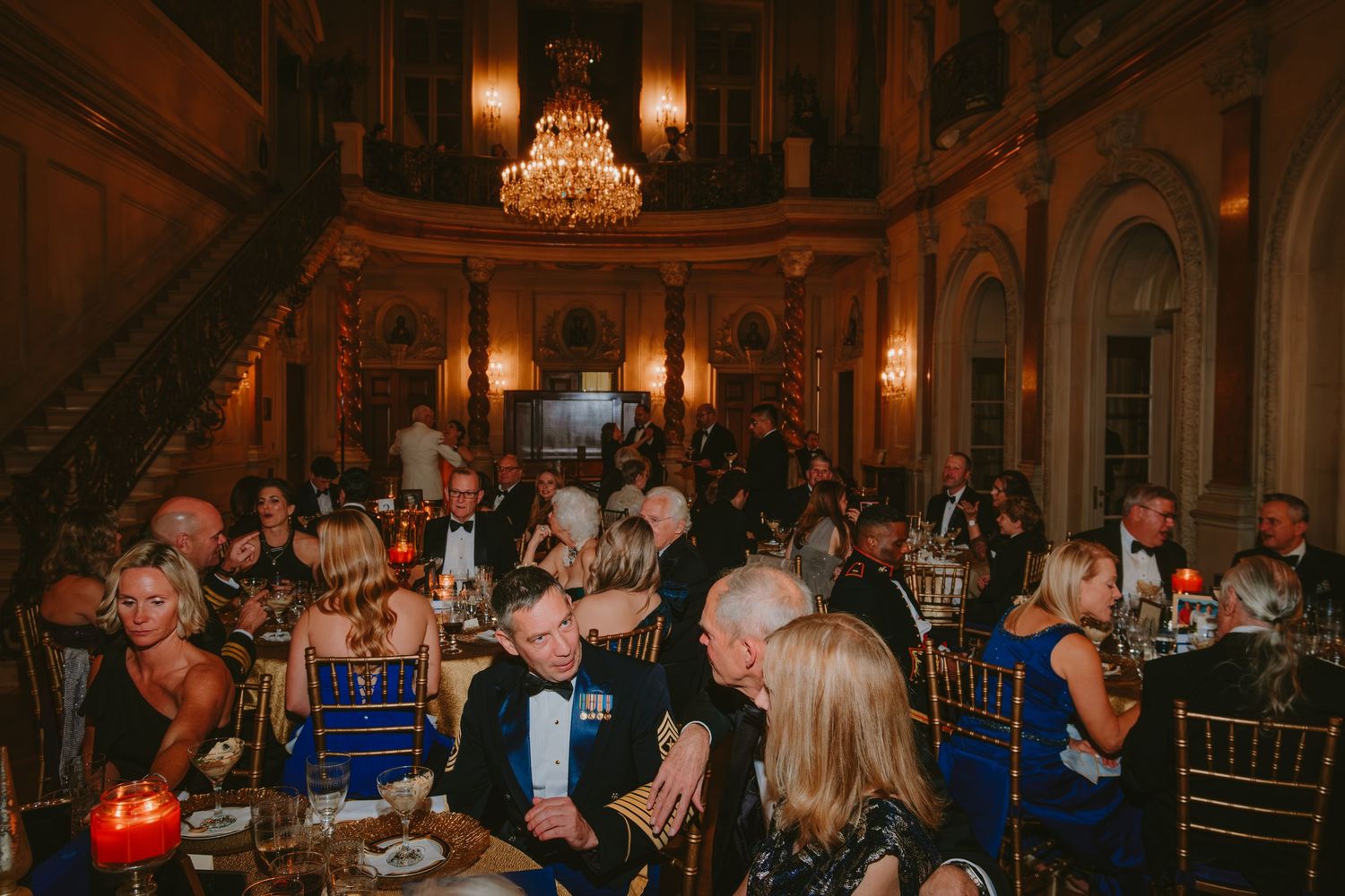 Elegant wedding reception with crystal chandelier illuminating a ballroom filled with guests at dining tables.